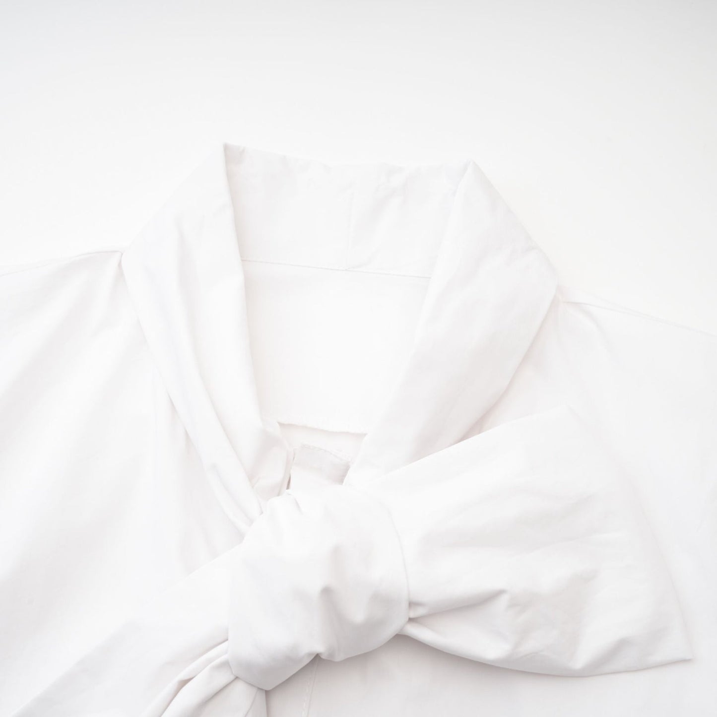 A white cotton buttonup shirt with long sleeves and a tie front detail named Solene