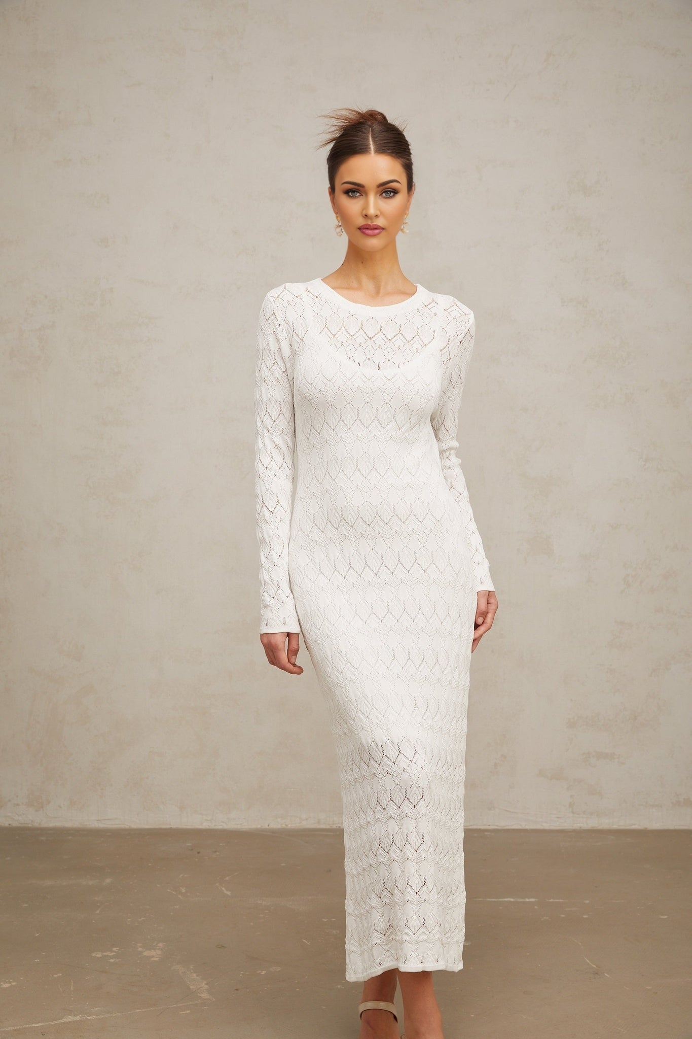 A white crochet knit midi dress with intricate lace patterns hanging on display