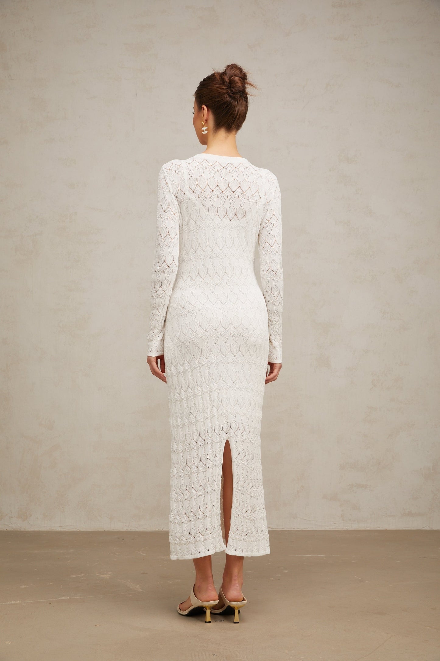 A white crochet knit midi dress with intricate lace patterns hanging on display