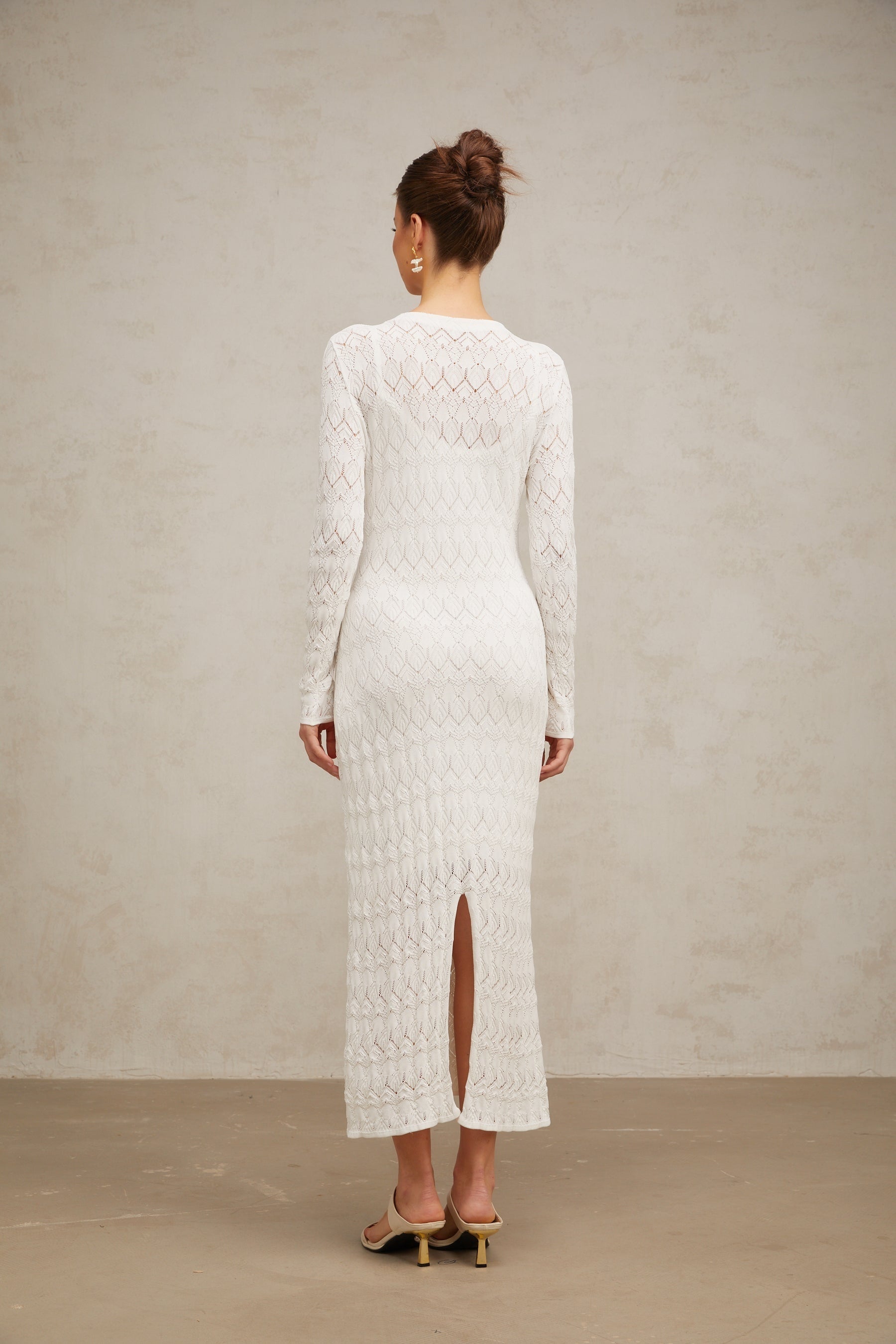 A white crochet knit midi dress with intricate lace patterns hanging on display