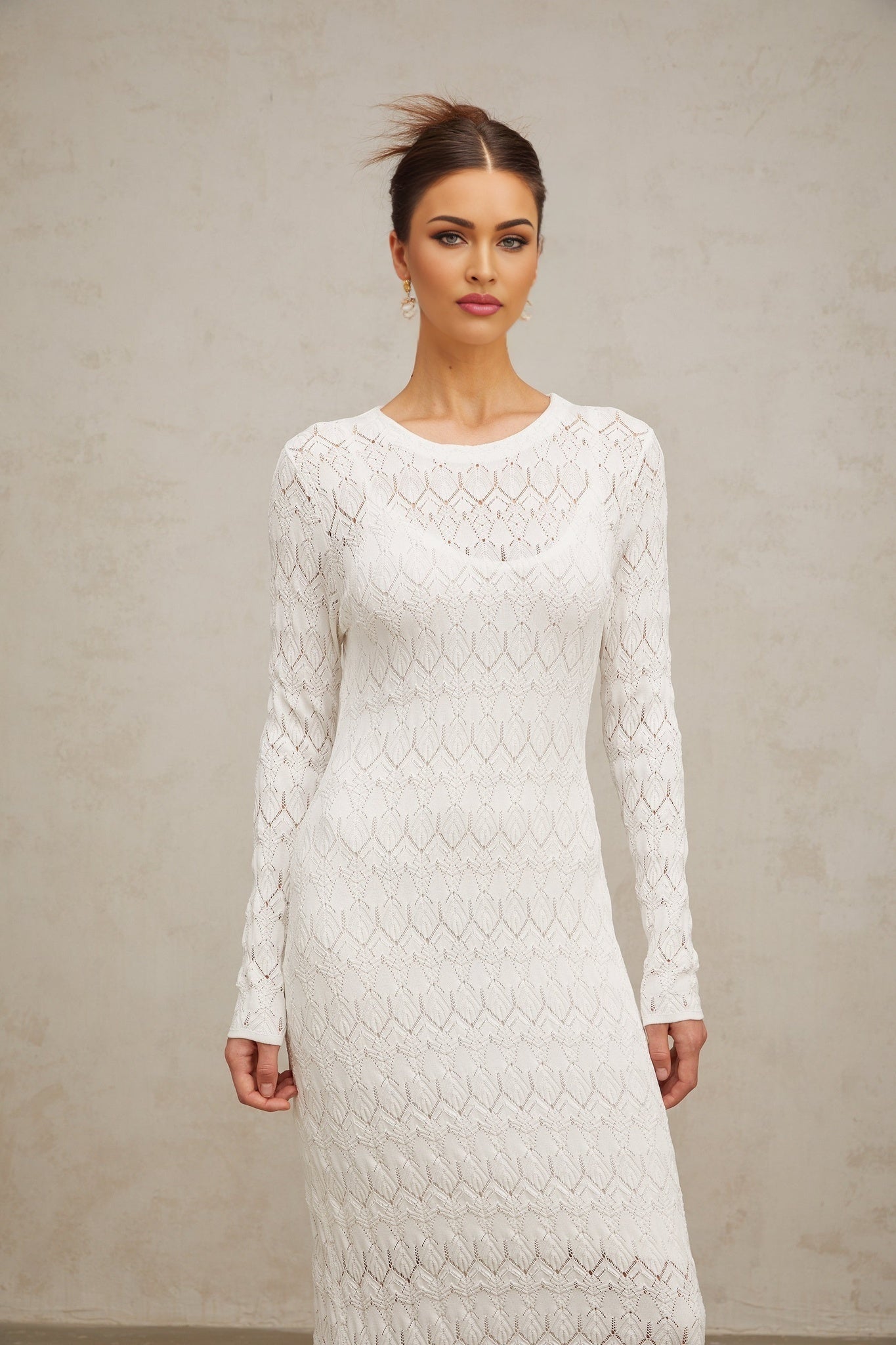 A white crochetknit midi dress with intricate patterns hanging on display showcasing its delicate texture and elegant silhouette