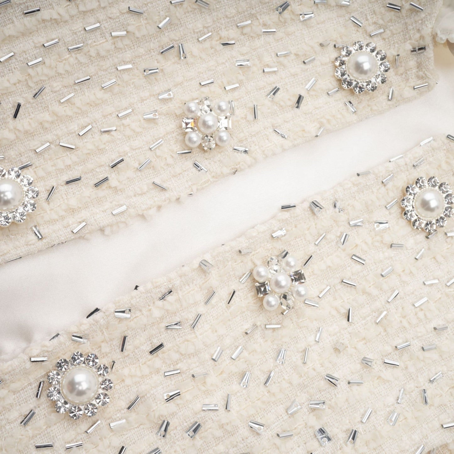A white cropped jacket with beaded details and ruffled trim worn by a model against a plain background