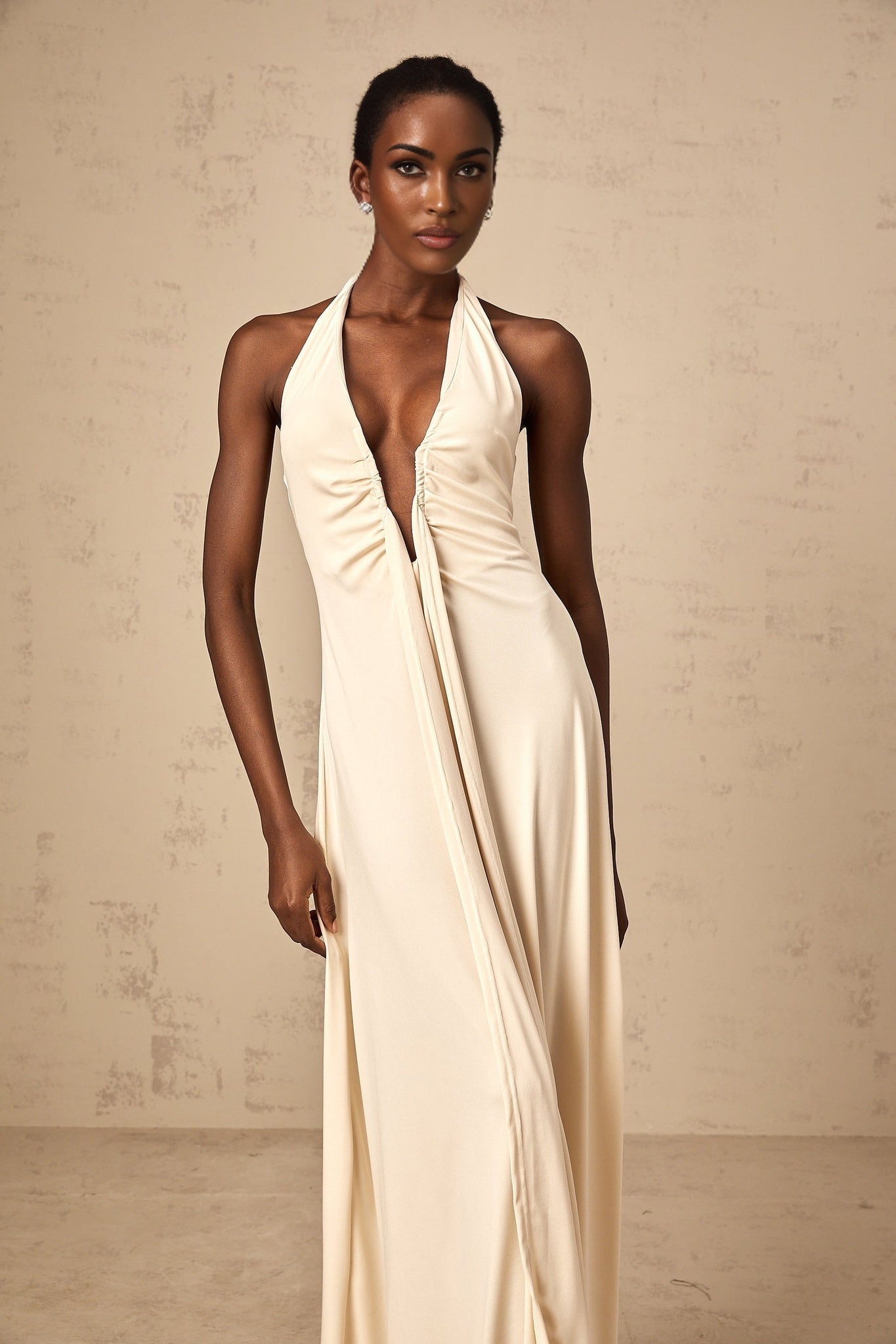 A white floorlength maxi dress with a deep V neckline and draped fabric details worn by a model
