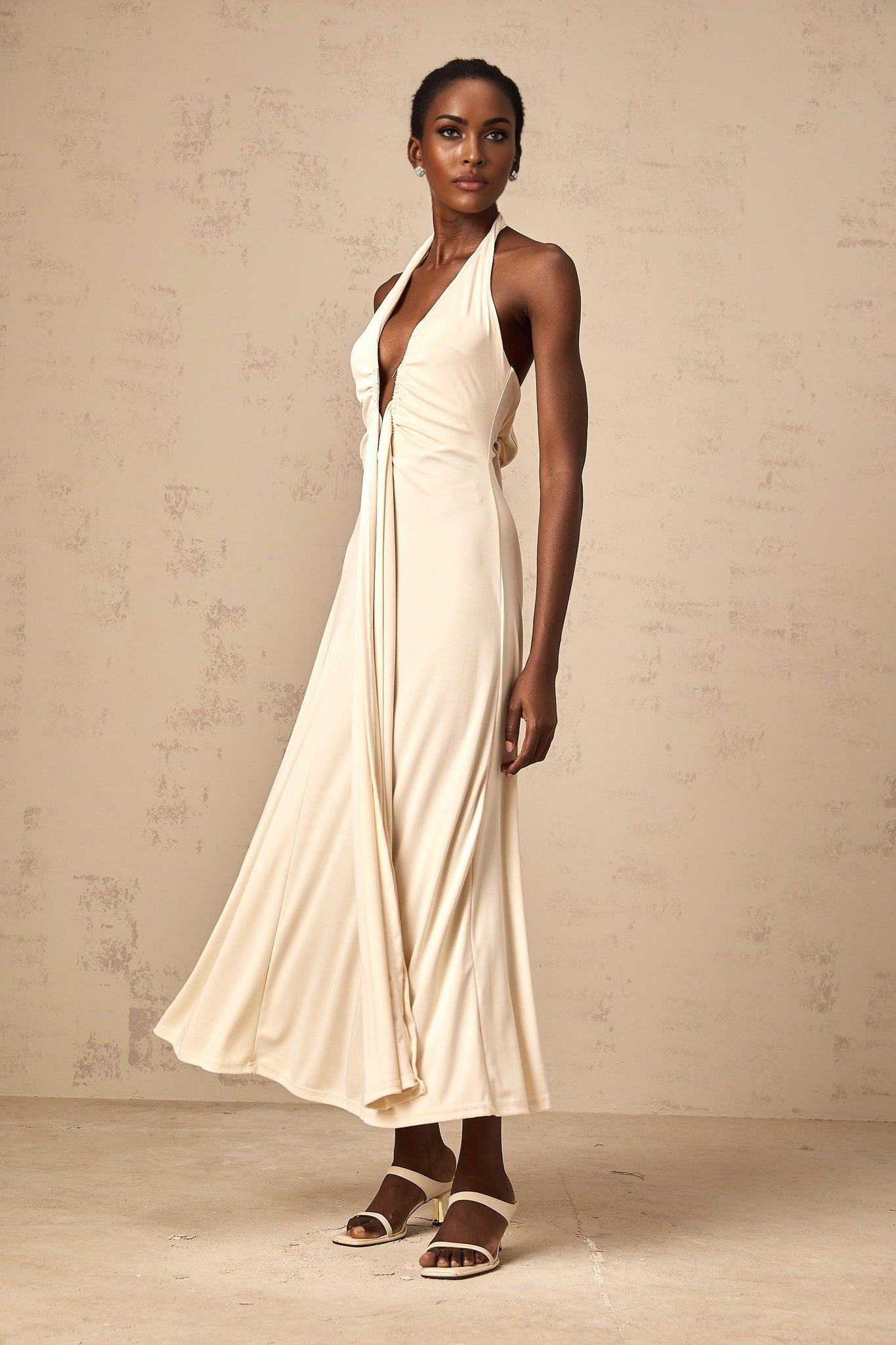 A white flowing maxi dress with a deep V neckline and draped fabric details worn by a model