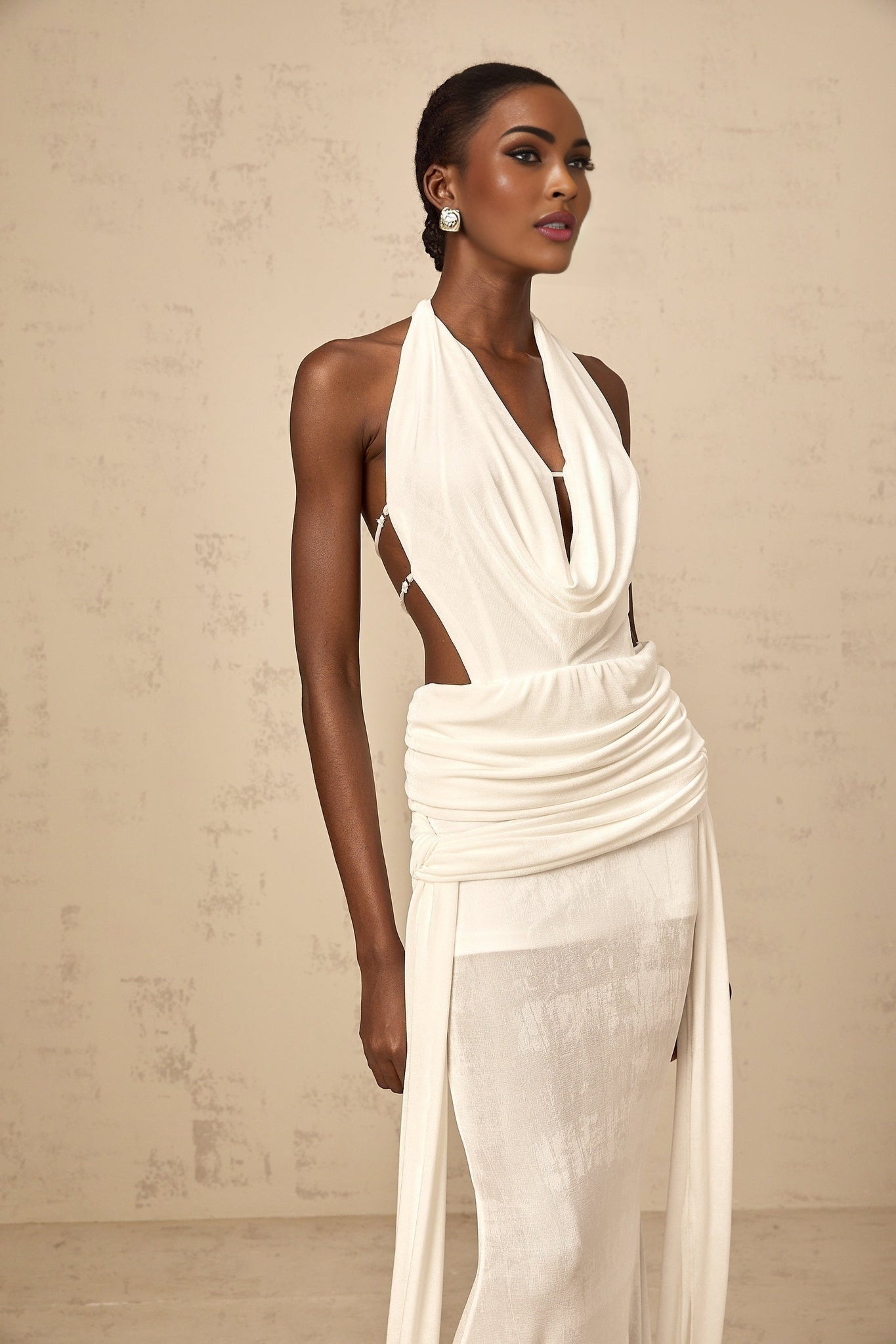 A white halterneck maxi dress with a backless design featuring a long flowing skirt and a tied neck closure