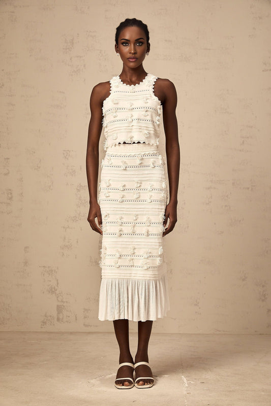 A white knit matching set consisting of a top and skirt with pointelle trim detailing Paola brand clothing displayed on a plain background