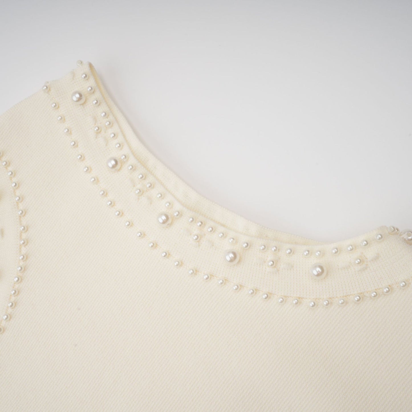 A white knitted maxi dress with faux pearl embellishments worn by a model standing against a plain background