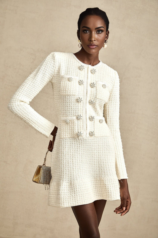 A white knitted mini dress with a flared skirt design named Liane worn by a model against a plain background