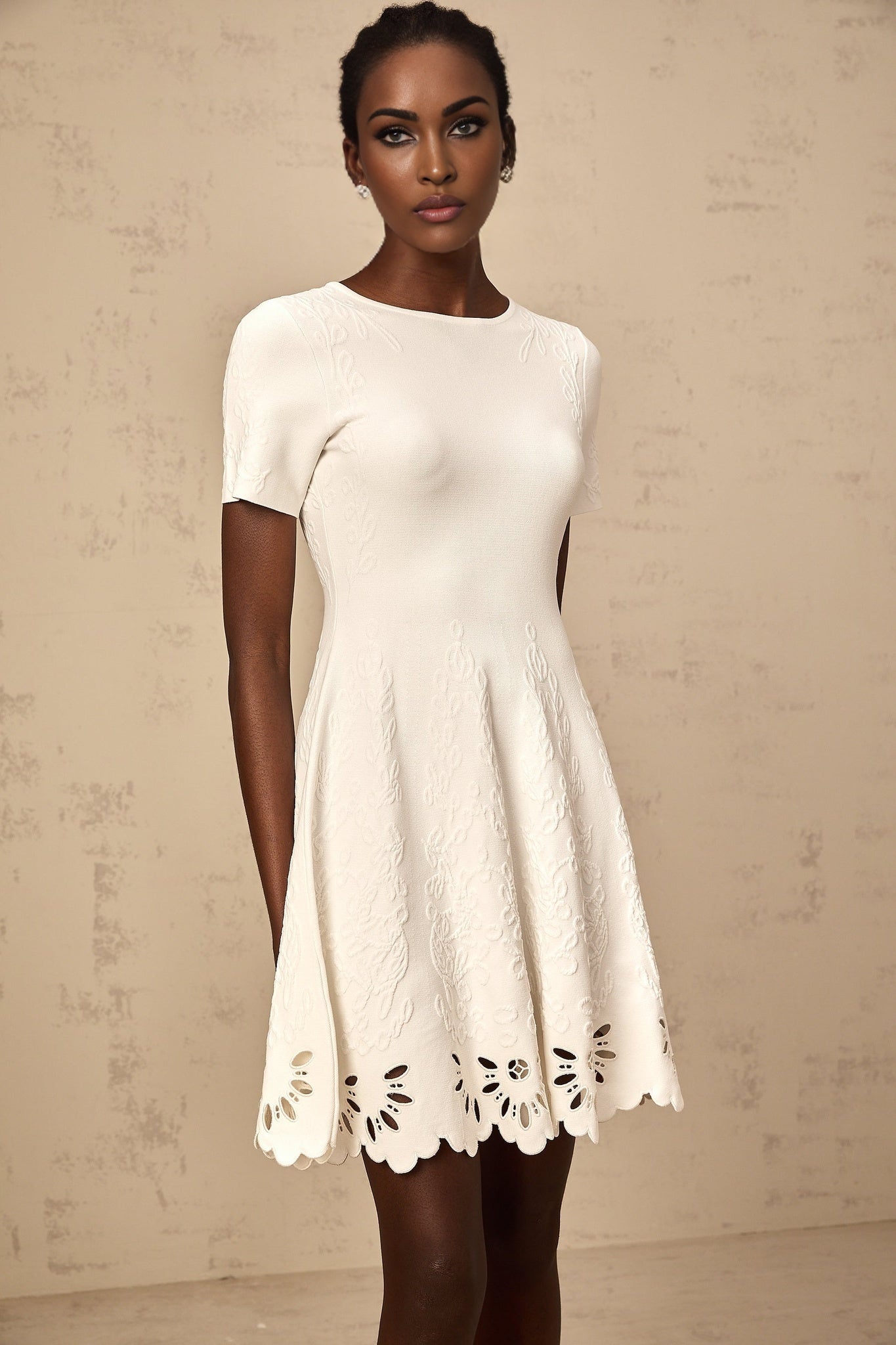 A white knitted mini dress with cut out jacquard detailing named Emilie showcasing a fitted silhouette and textured pattern