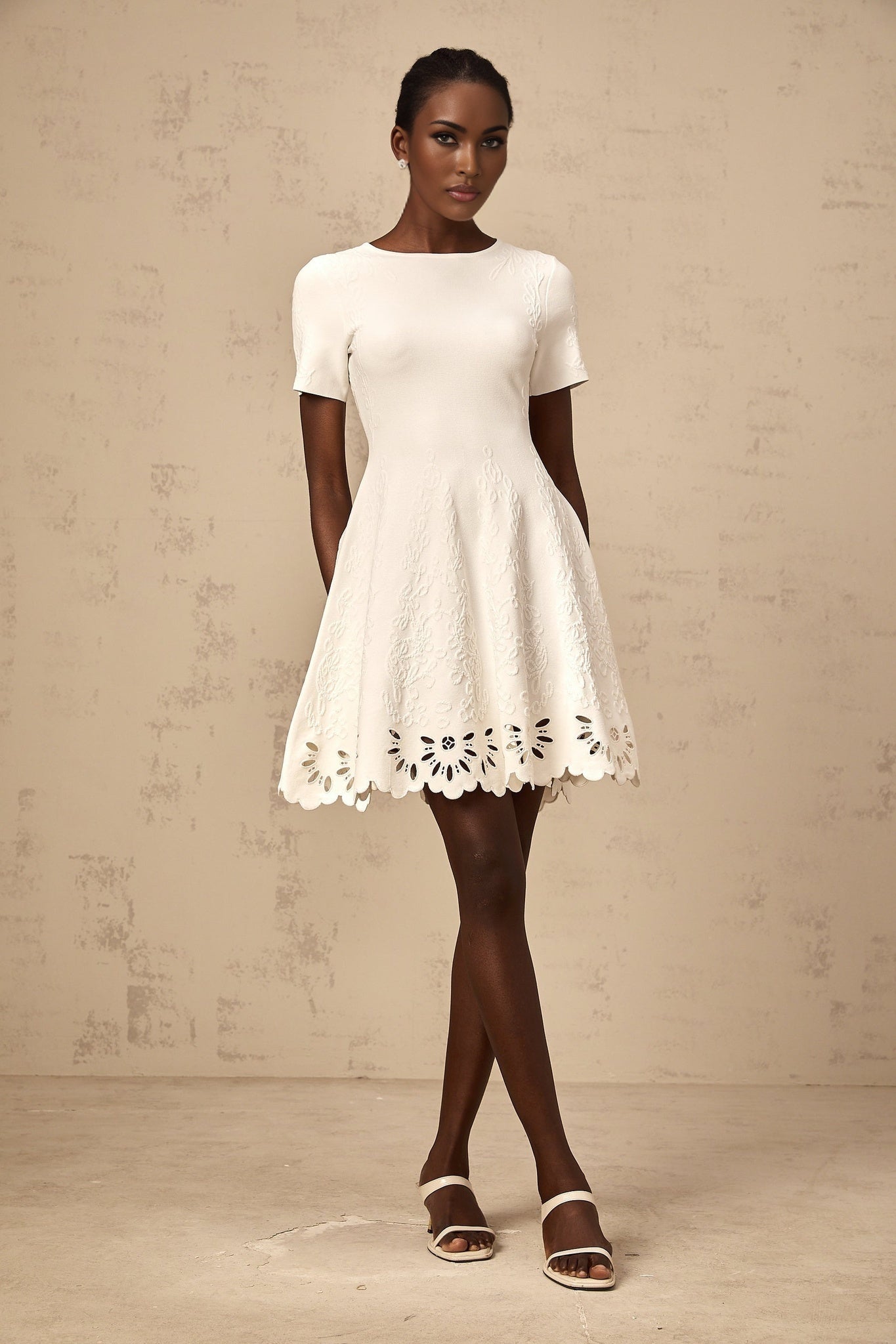 A white knitted mini dress with cut out jacquard detailing worn by a model named Emilie