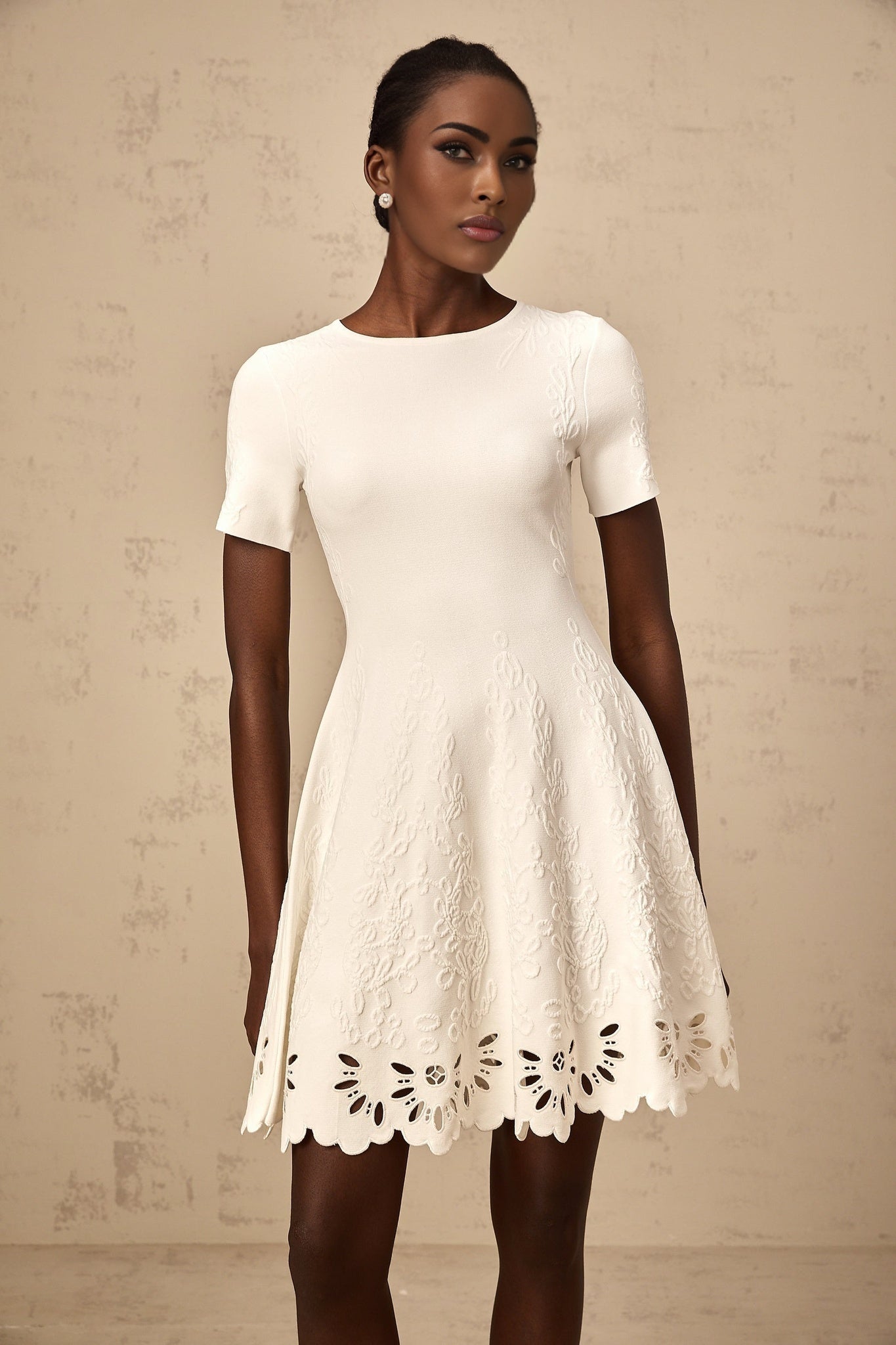 A white knitted mini dress with cut out jacquard pattern featuring a short hemline and intricate textured design