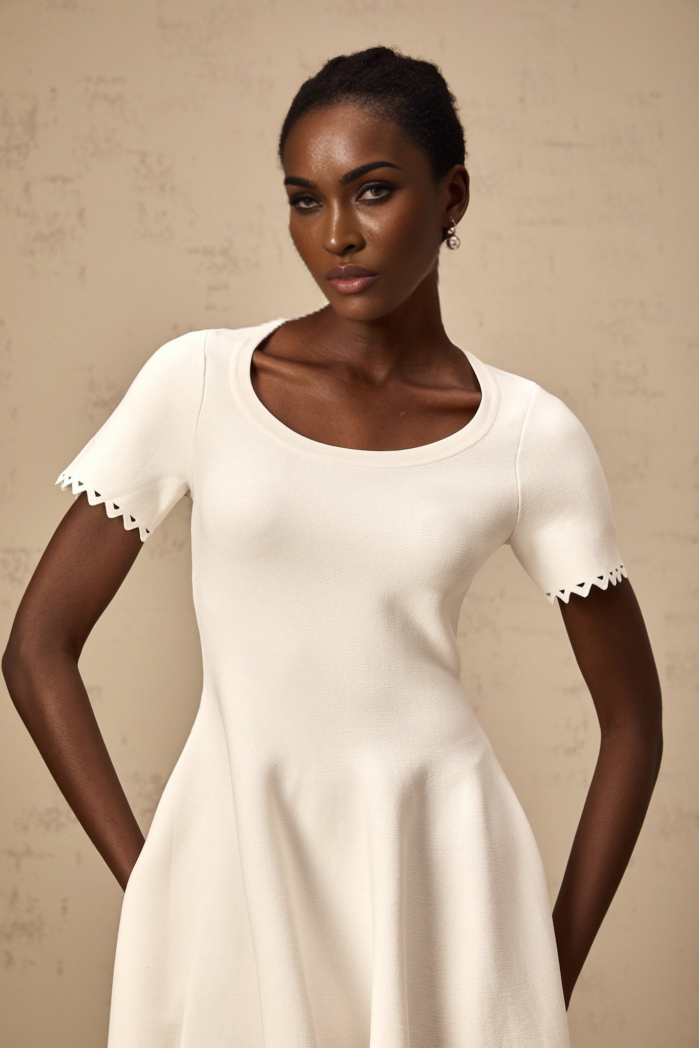 A white knitted mini dress with cutout details and a fleur design featuring a short hemline and fitted silhouette