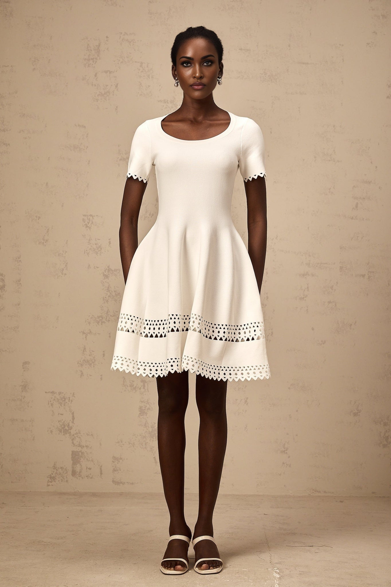 A white knitted mini dress with cutout details featuring a fleur design pattern