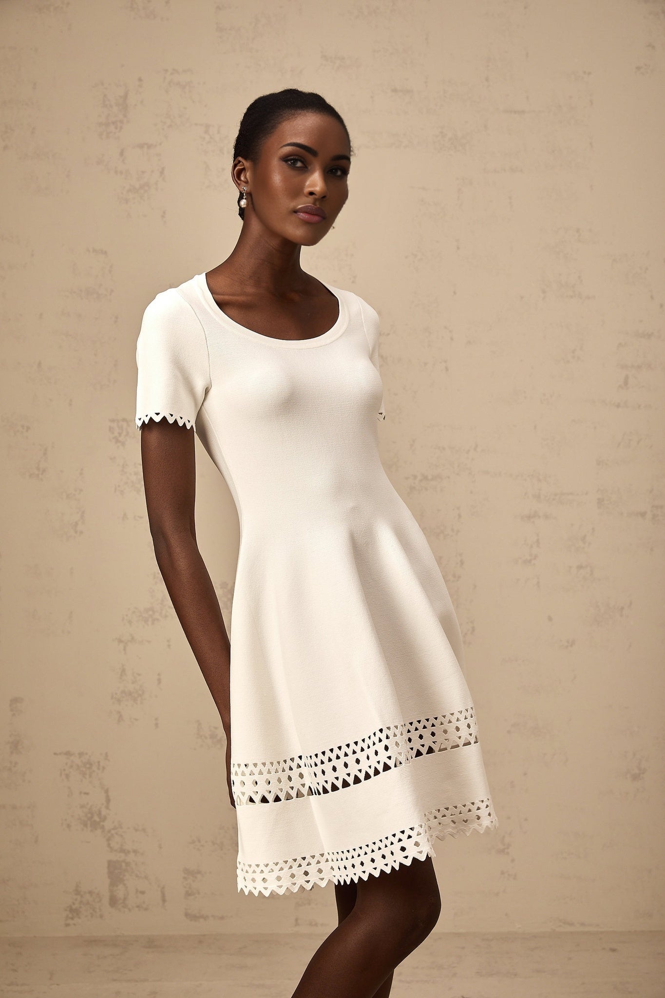 A white knitted mini dress with cutout details featuring a floral pattern and a short hemline