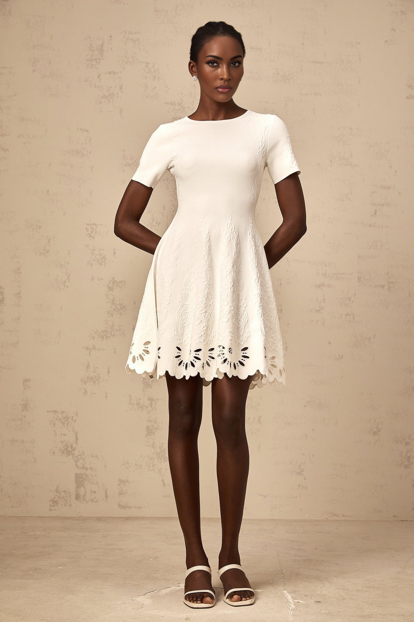 A white knitted mini dress with cutout jacquard pattern featuring a fitted silhouette and short hemline
