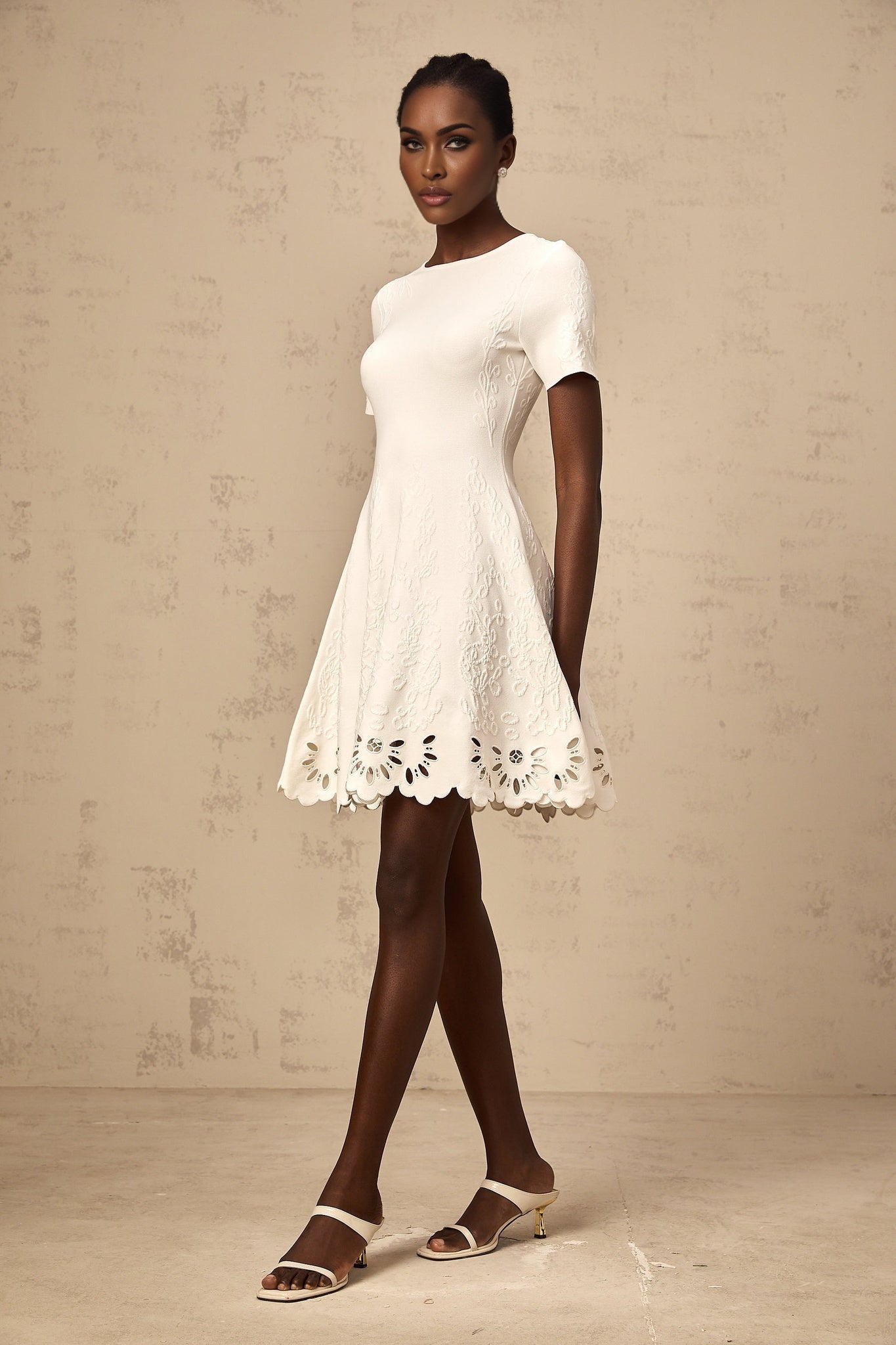 A white knitted mini dress with jacquard pattern and cutout details worn by a model named Émilie