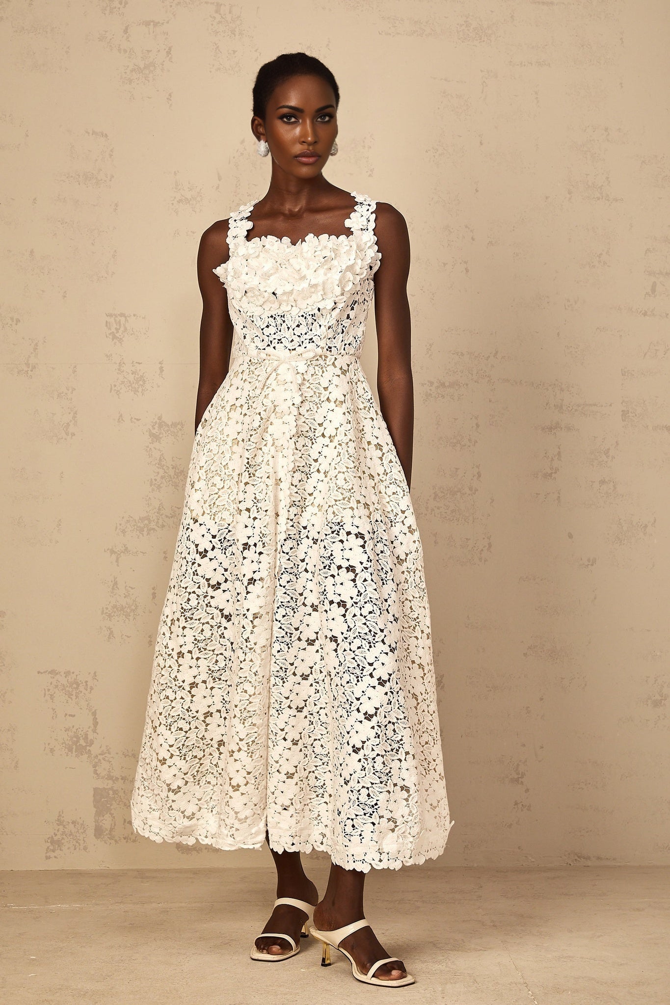 A white lace maxi dress with shirred detailing and corded lace pattern worn by a woman standing in a relaxed pose