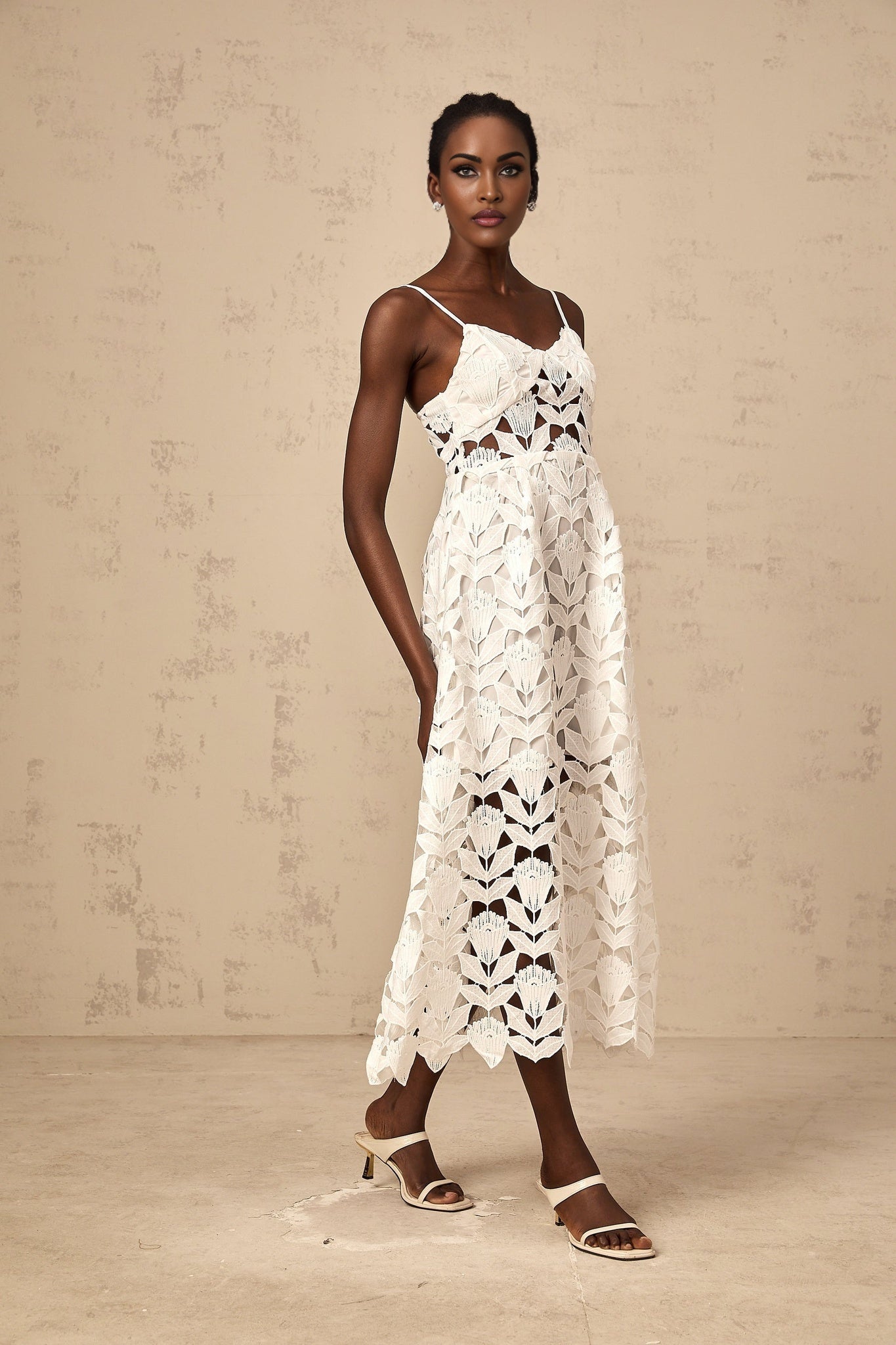 A white lace midi dress with cut out details featuring a delicate floral pattern and a fitted silhouette