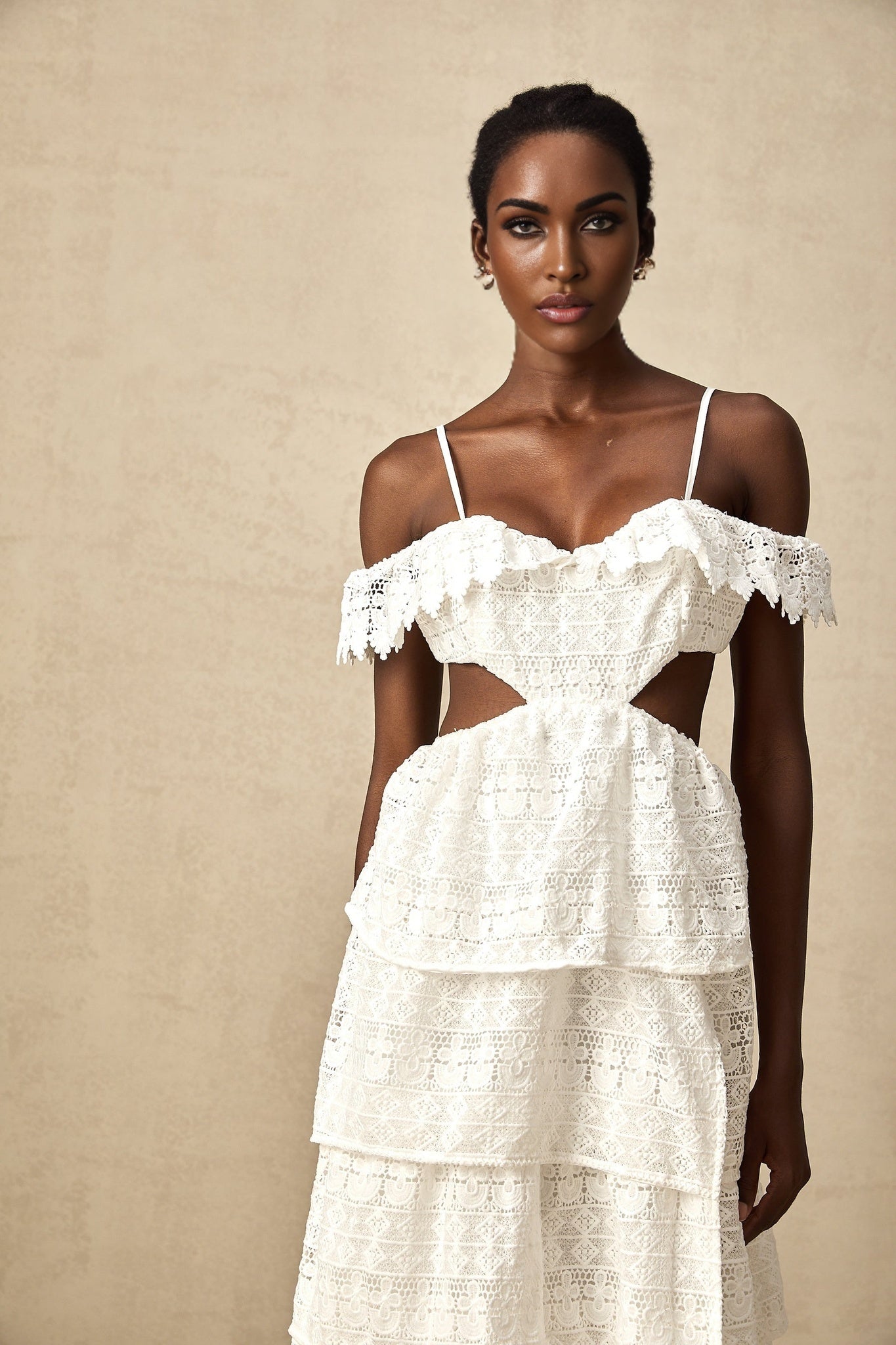A white lace midi dress with open work detailing named Genevieve worn by a model standing against a plain background