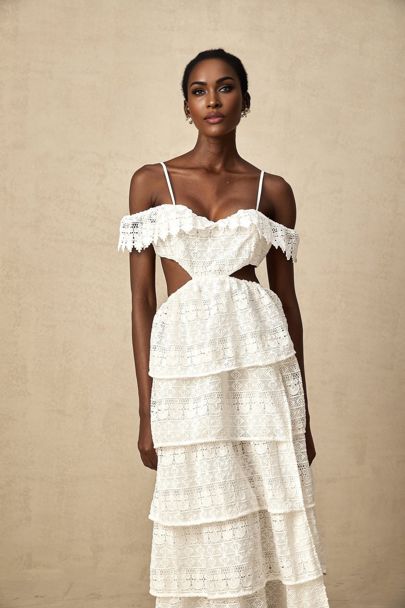 A white lace midi dress with openwork detailing named Genevieve worn by a model standing against a plain background