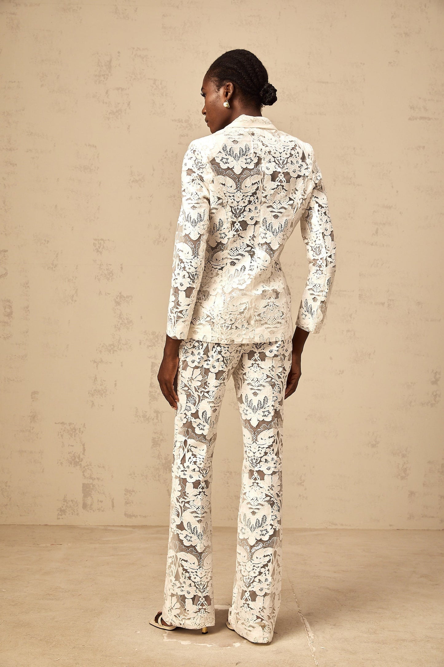 A white matching set featuring a blazer and trousers made of tulle with sequined flower embroidery The set is named Yaelle and has a delicate elegant appearance