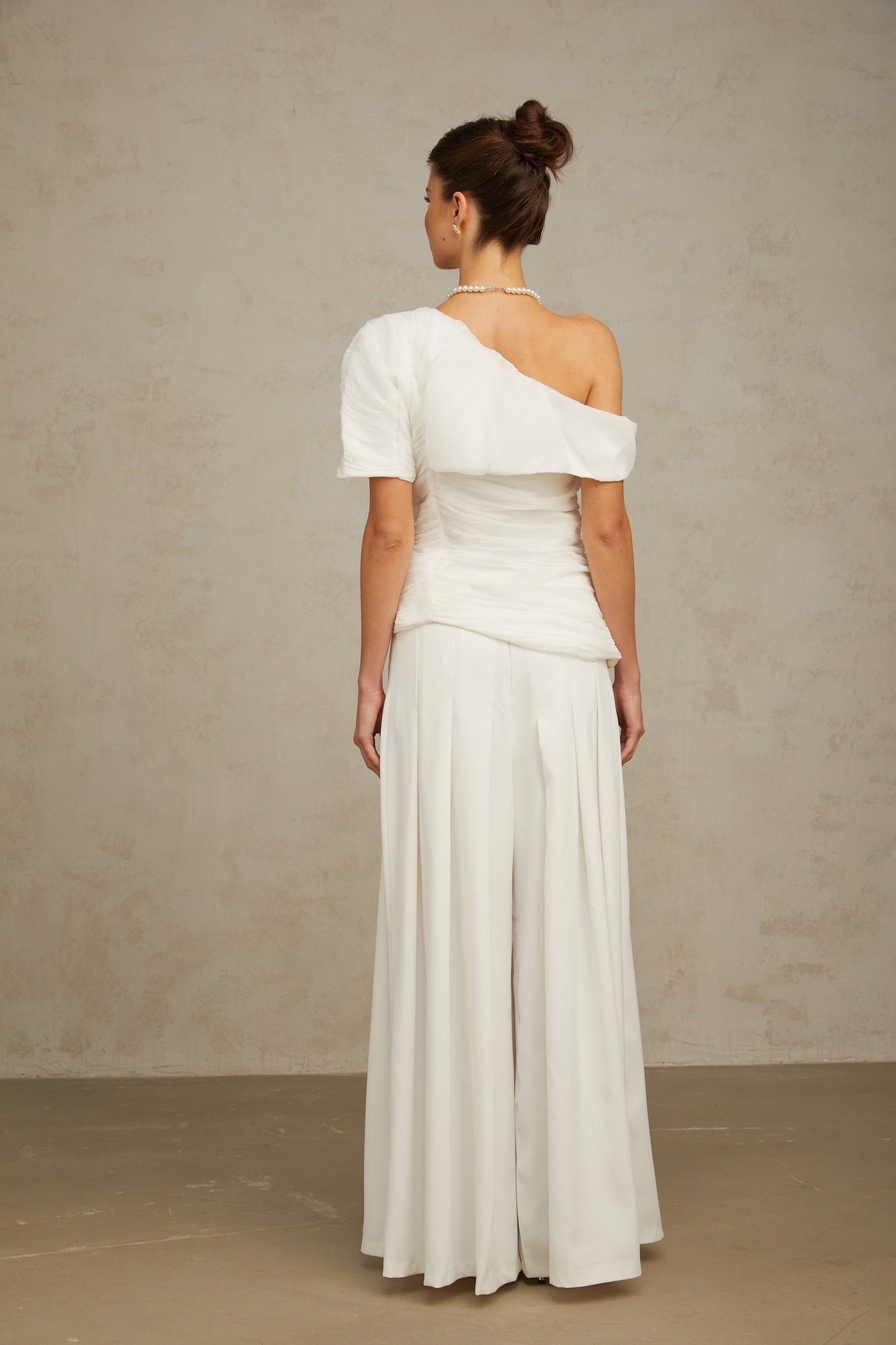 A white matching set featuring a creased top and trousers worn by a model against a plain background