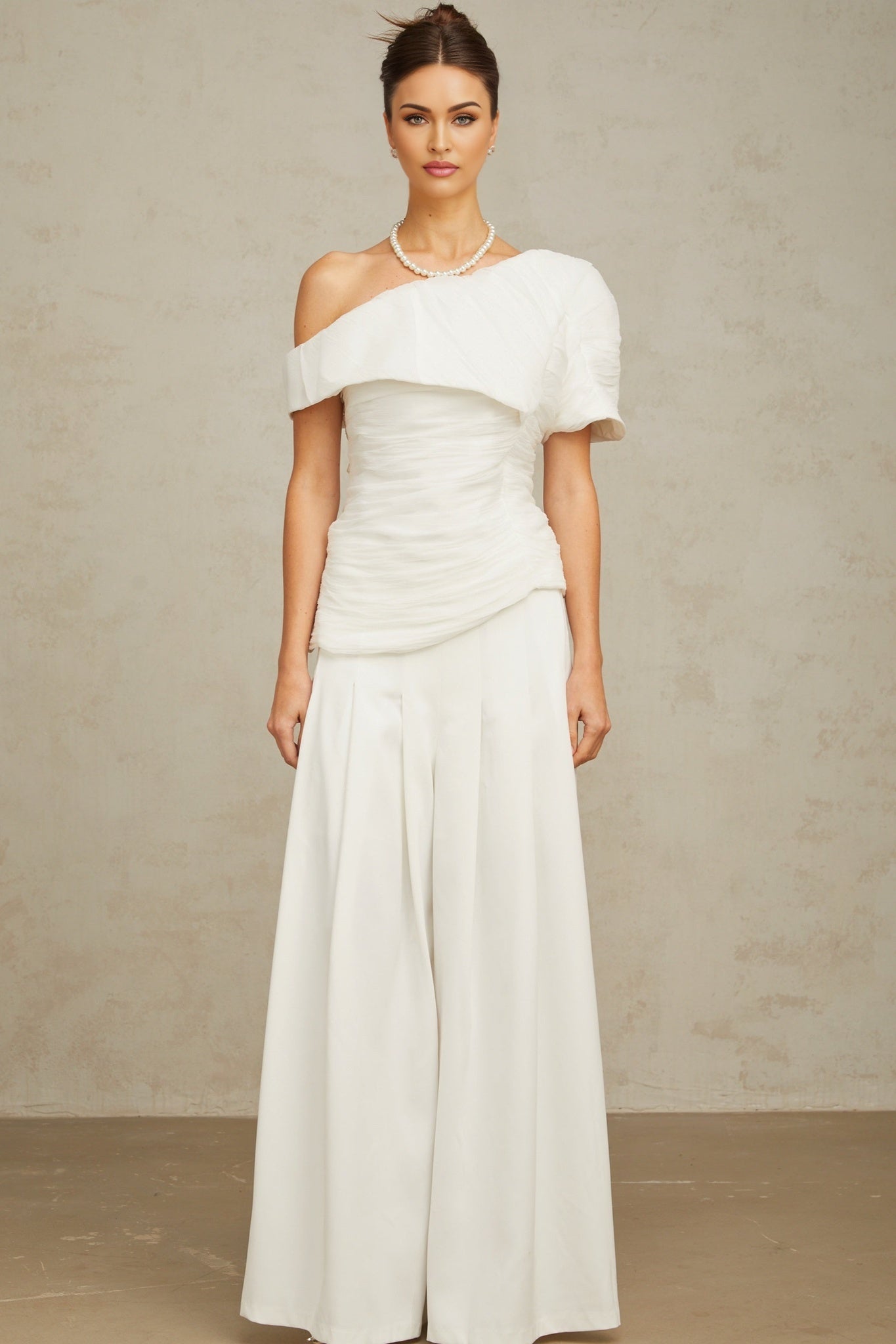 A white matching set featuring a creased top and trousers worn by a model standing against a plain background