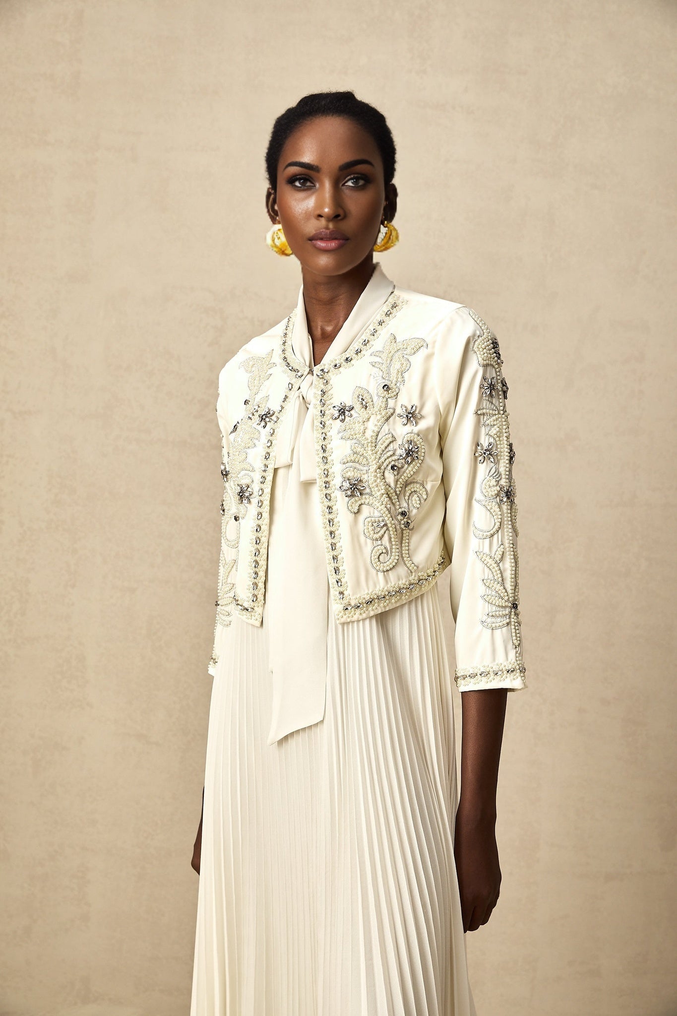 A white matching set featuring a pleated jacket and dress with embellishments The jacket has a fitted silhouette and the dress is sleeveless Both pieces are adorned with delicate embellishments creating an elegant and coordinated look