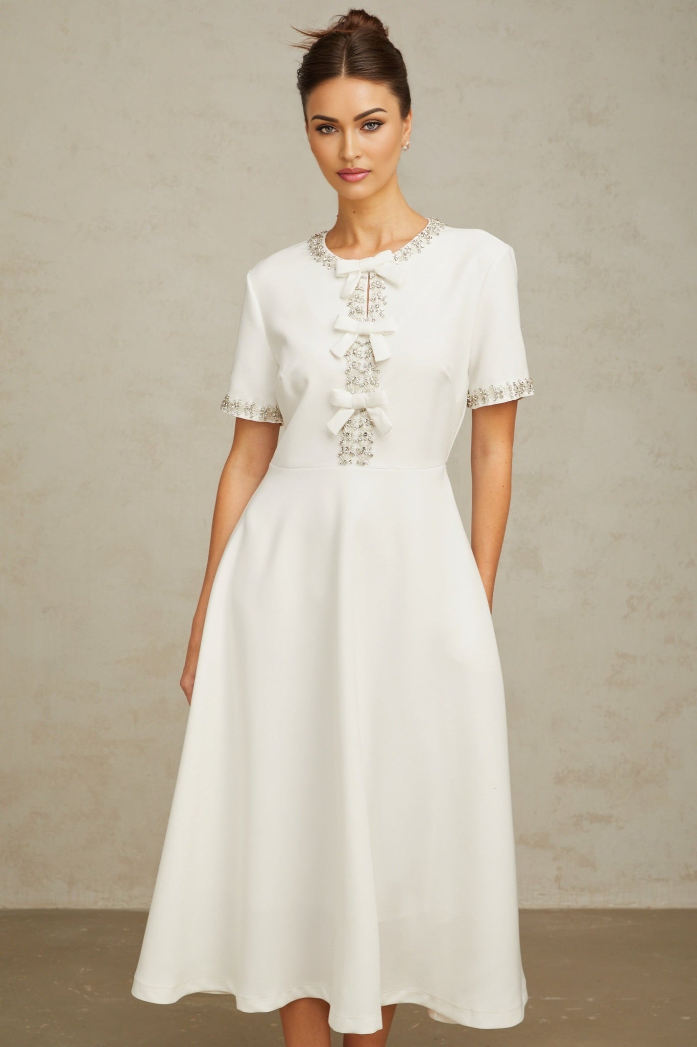 A white midi dress featuring a crystalaccented bow detail and a fitted silhouette named Cassiopeia