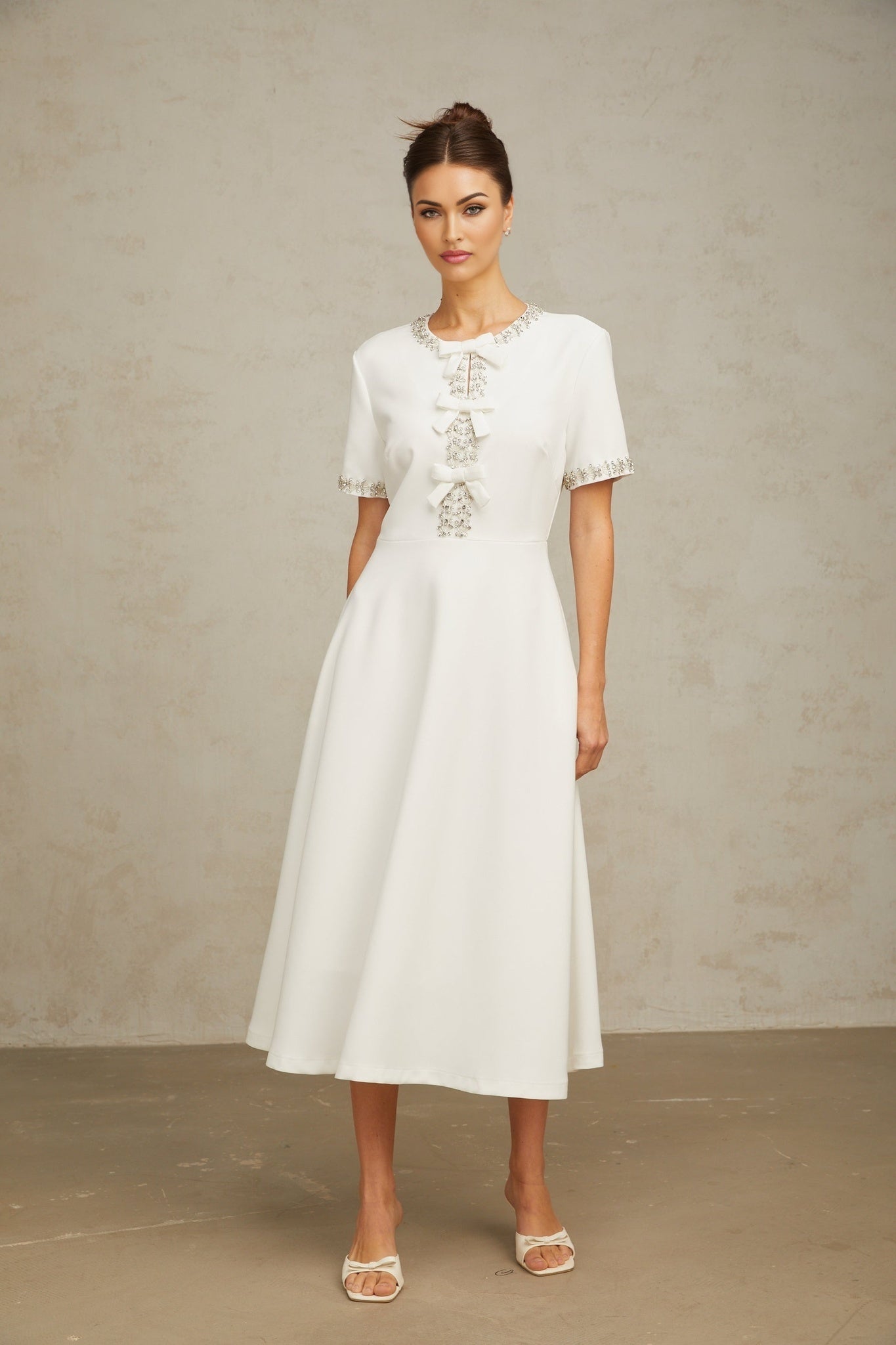A white midi dress featuring a crystalaccented bow detail and a sleek silhouette inspired by the Cassiopeia constellation