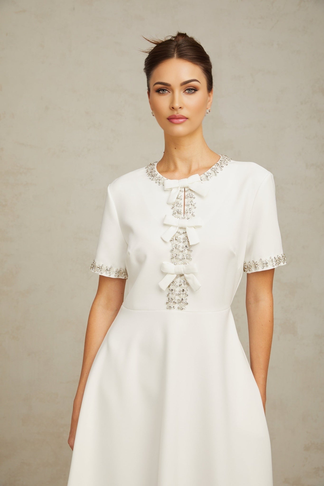 A white midi dress featuring crystal accents and a bow detail showcasing the Cassiopeia design