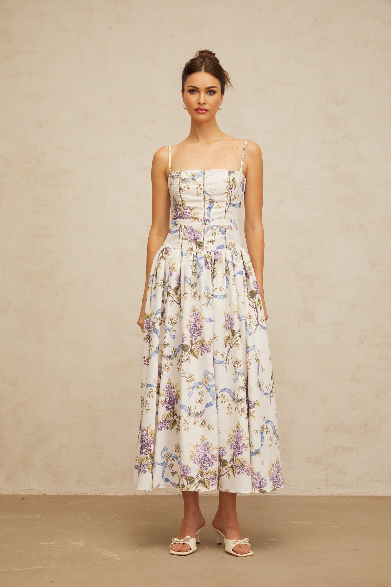 A white midi dress with a floral print pattern covering the fabric The dress features a feminine silhouette and delicate floral motifs in various colors against the white background
