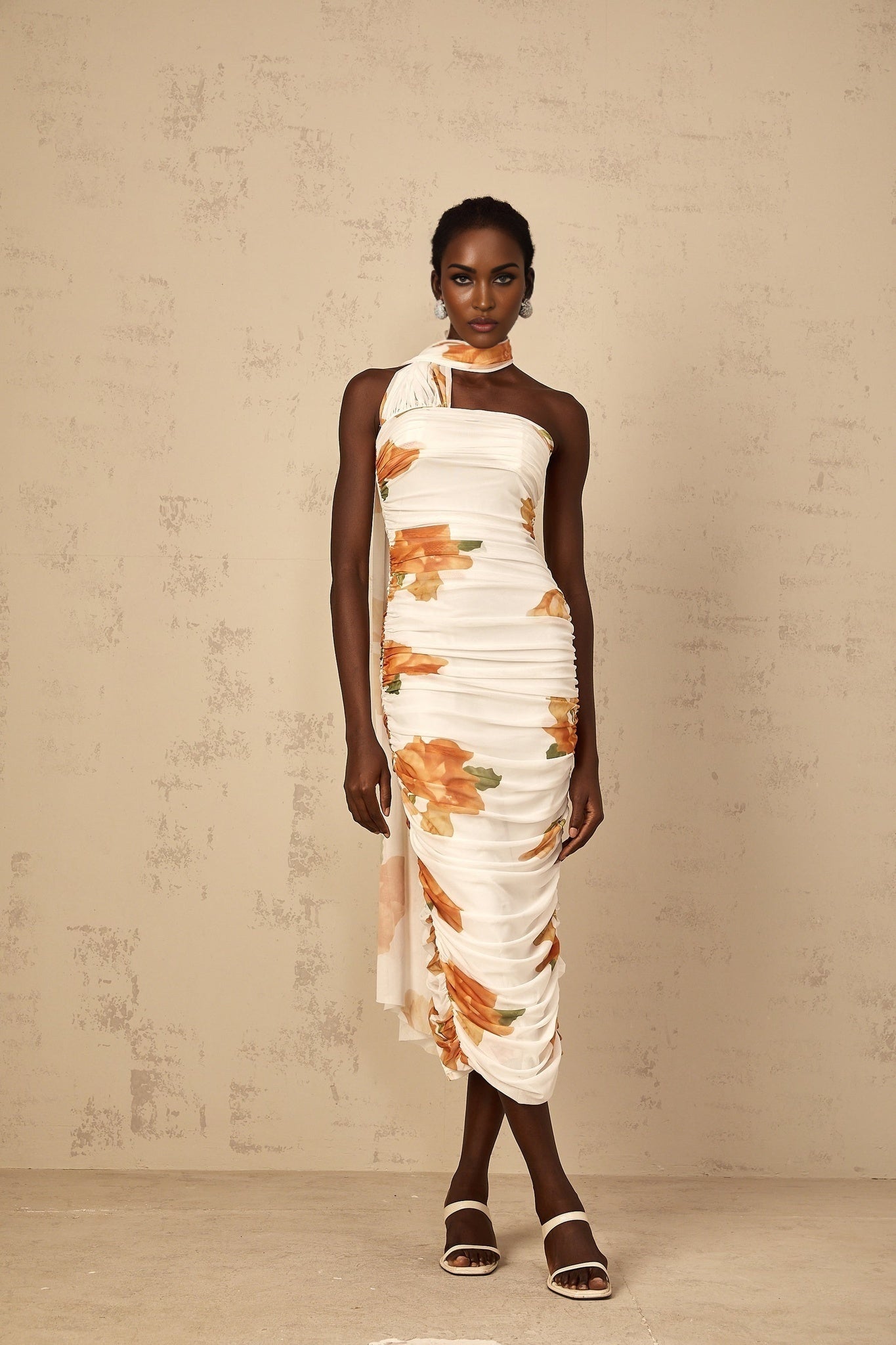 A white midi dress with a floral print pattern made of ruched tulle fabric featuring a fitted bodice and flowing skirt