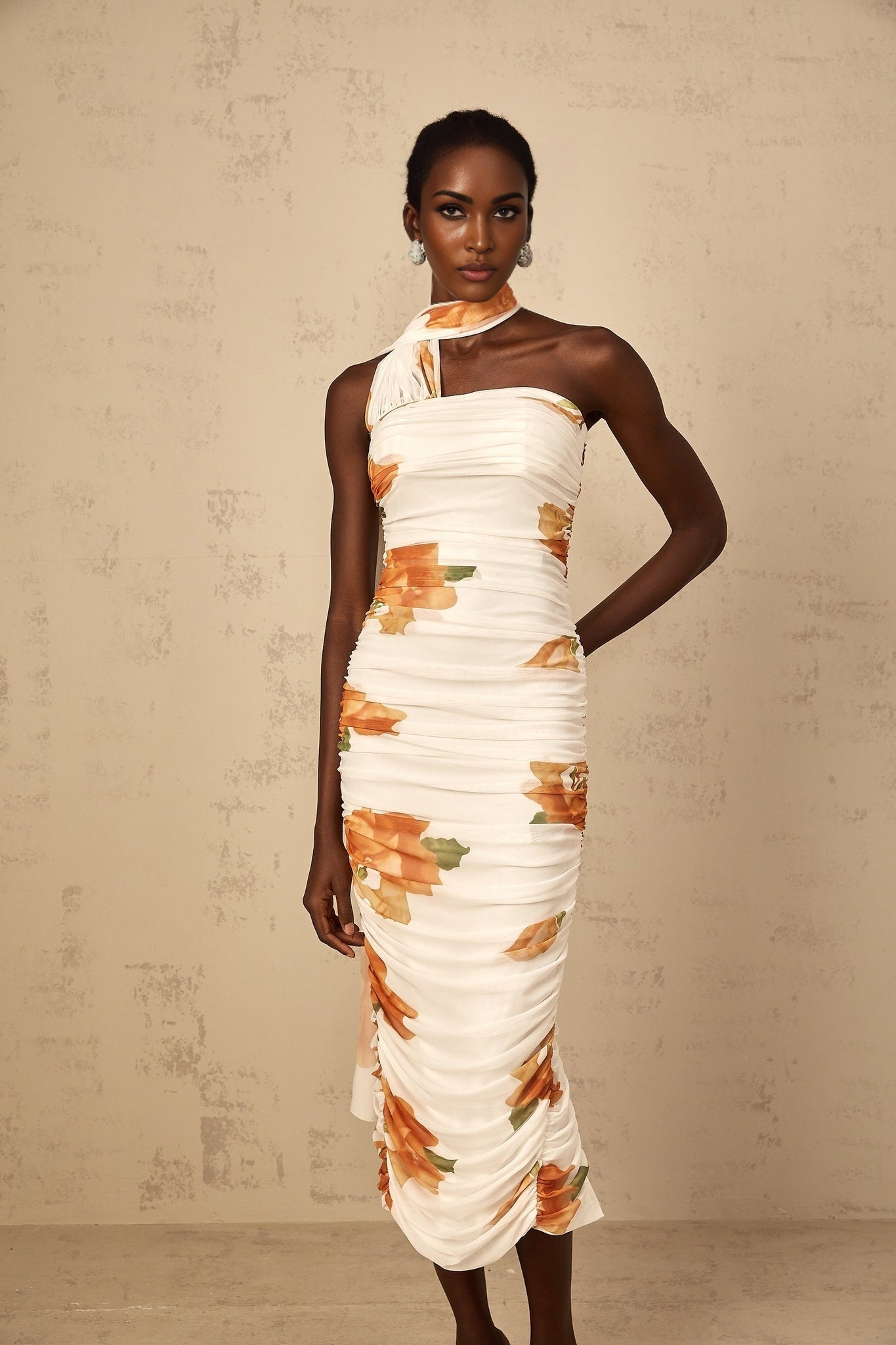 A white midi dress with a floral print pattern made of ruched tulle fabric featuring a fitted bodice and flowing skirt