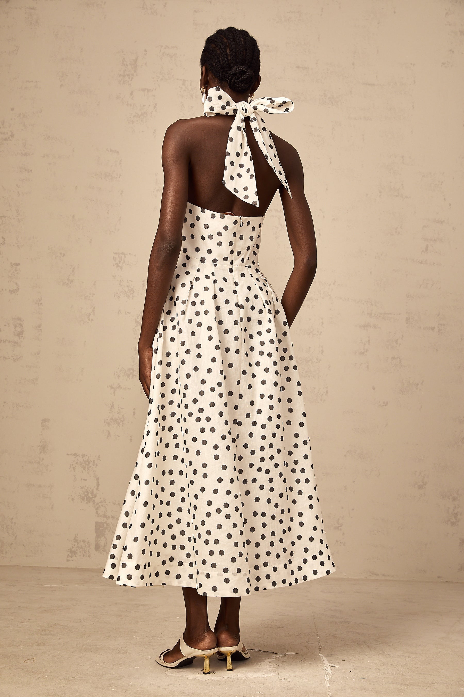 A white midi dress with black polka dots and a bow detail at the neckline named Audrey