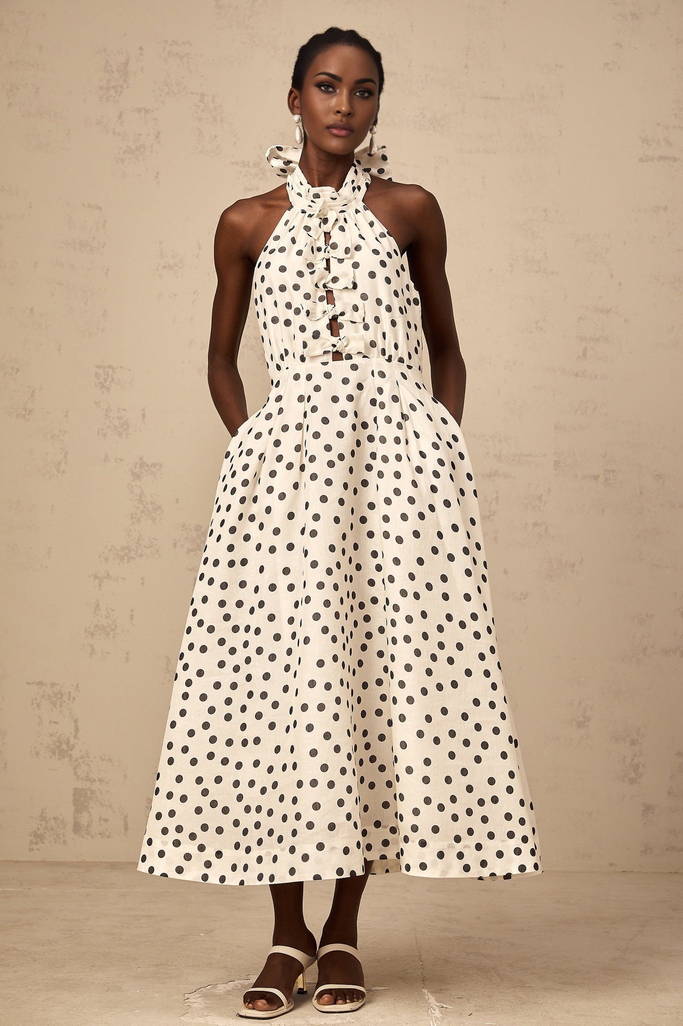 A white midi dress with black polka dots featuring a bow detail and named Audrey