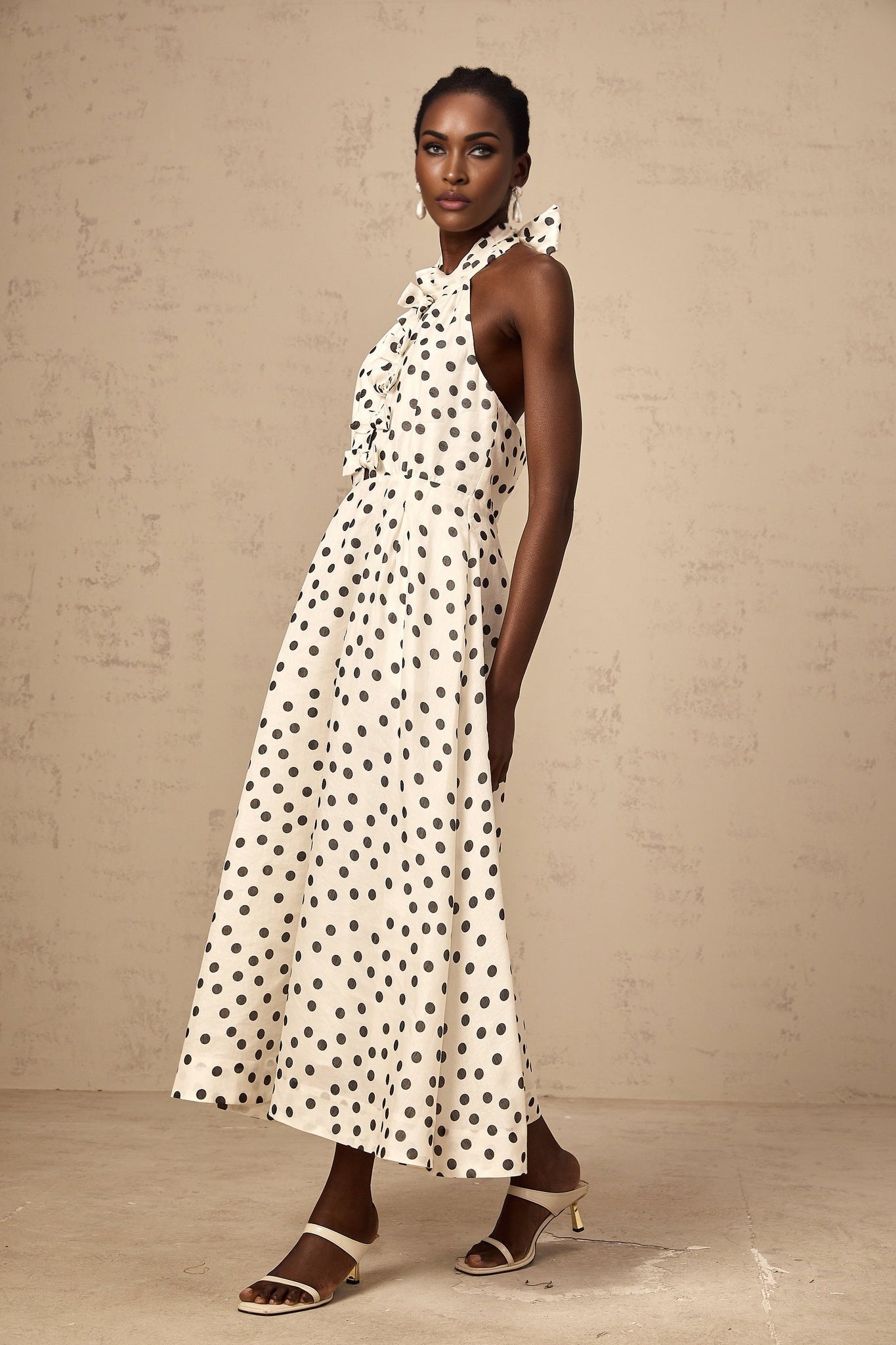 A white midi dress with black polka dots featuring a bow detail and named Audrey