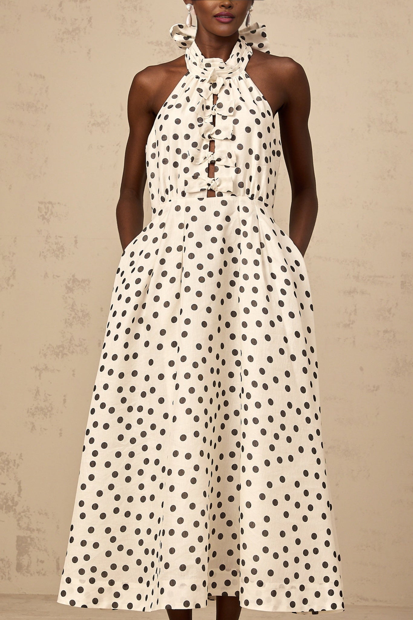 A white midi dress with black polka dots featuring a bow detail at the waist named Audrey