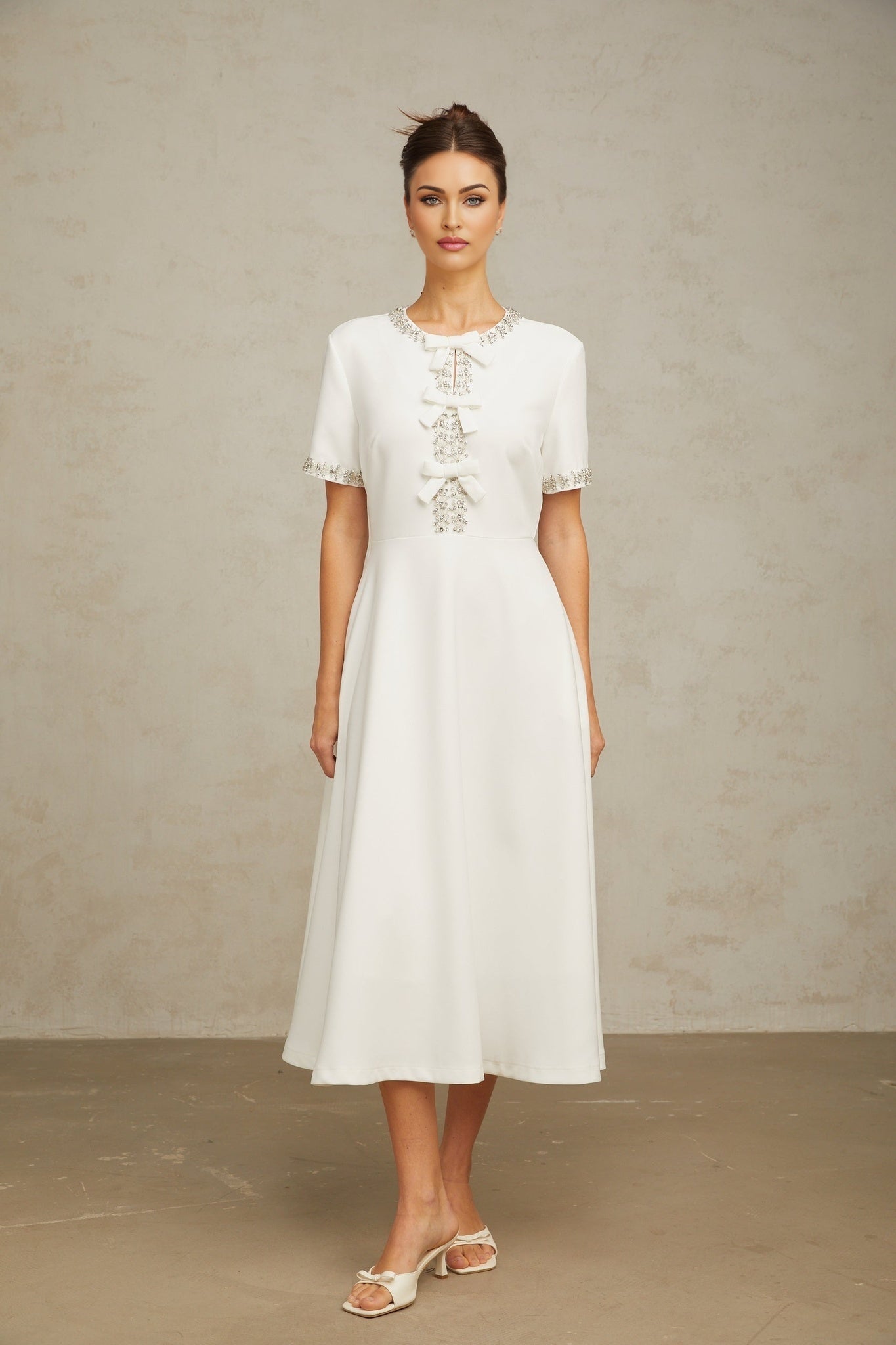 A white midi dress with crystal accents and a bow detail inspired by the Cassiopeia constellation