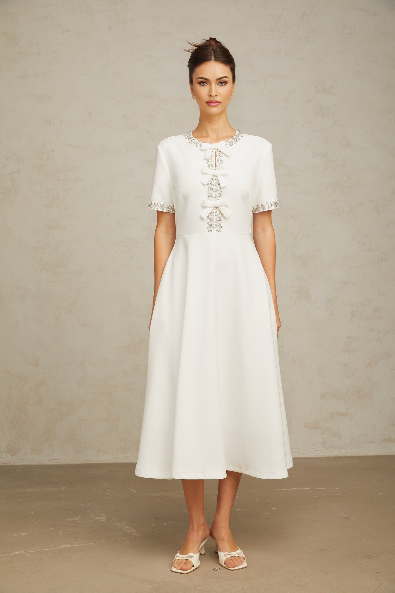 A white midi dress with crystal accents and a bow detail named Cassiopeia