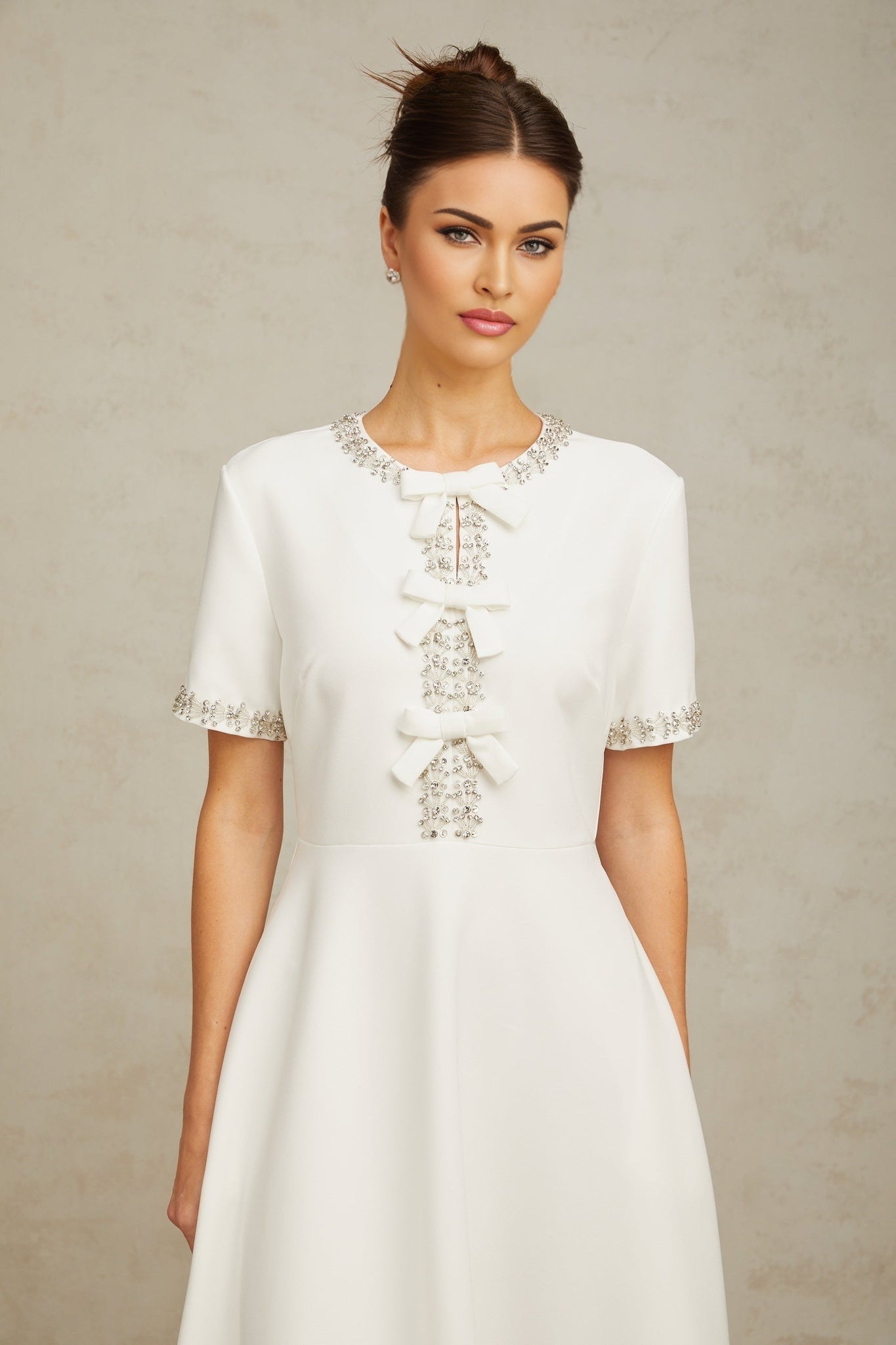 A white midi dress with crystal accents and a bow detail named Cassiopeia