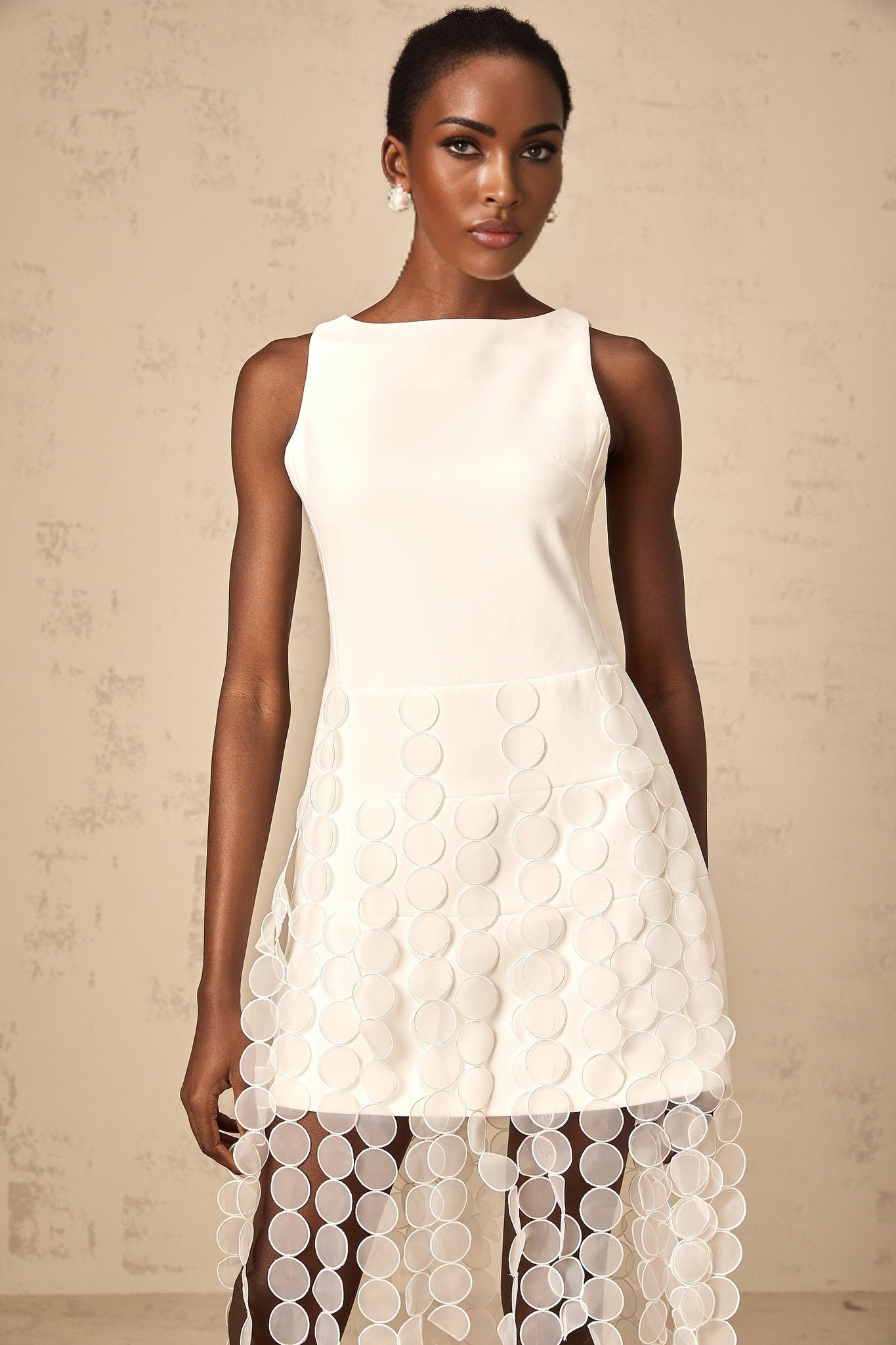 A white midi dress with discshaped designs and fringe detailing worn by a model named Justine
