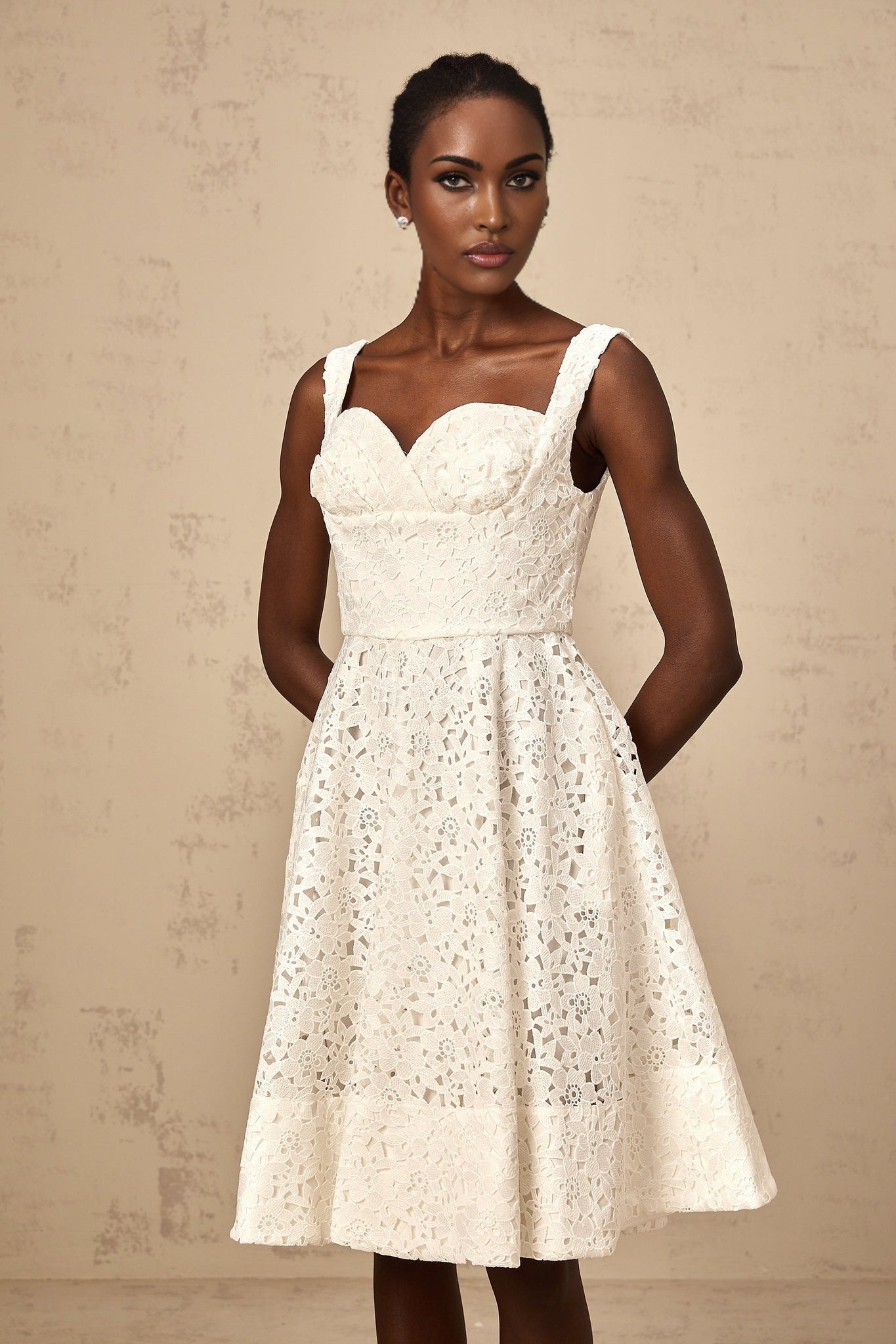 A white midi dress with floral lace pattern worn by a model standing against a plain background