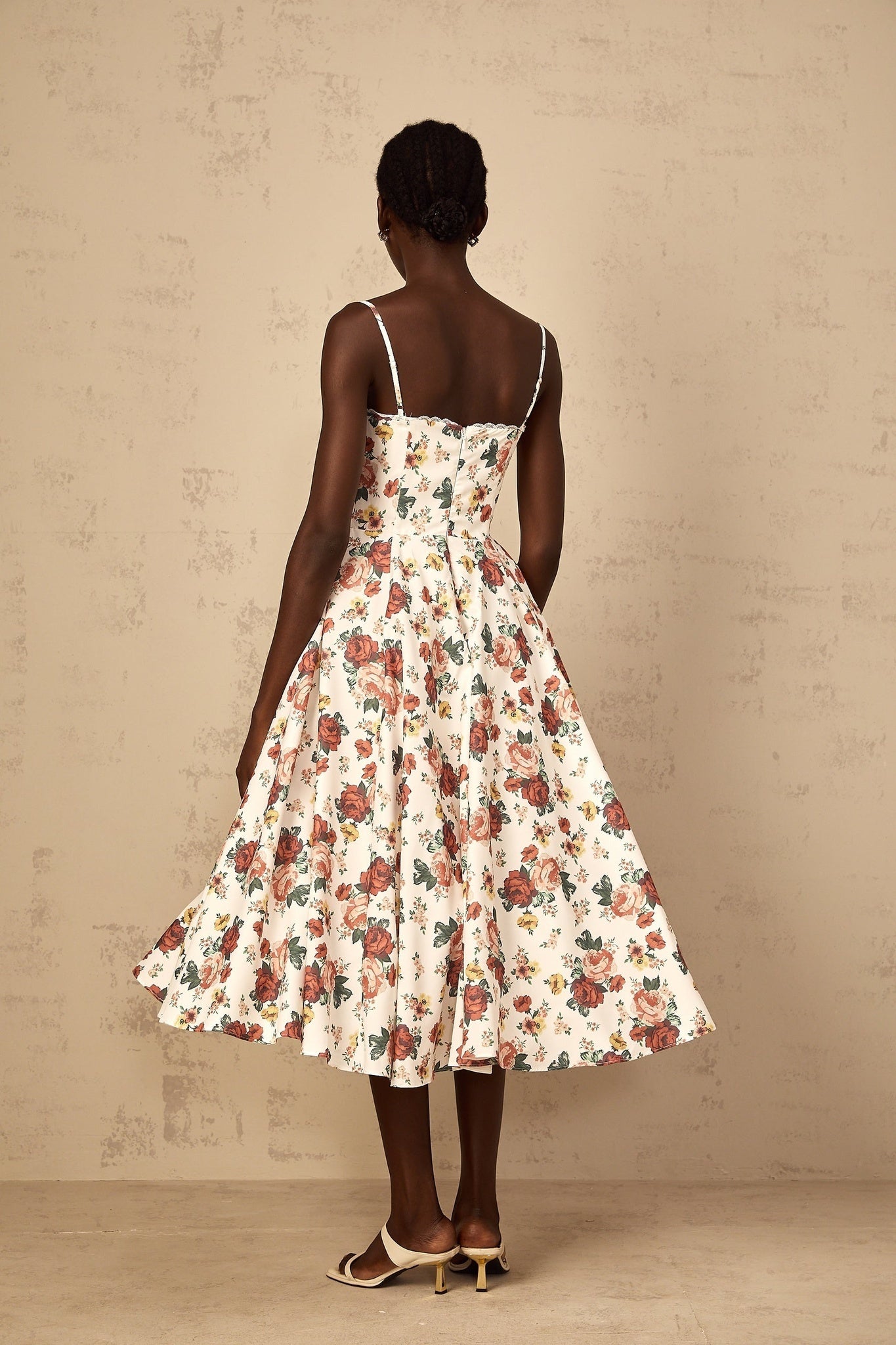 A white midi dress with rose print pattern featuring flounced details worn by a woman
