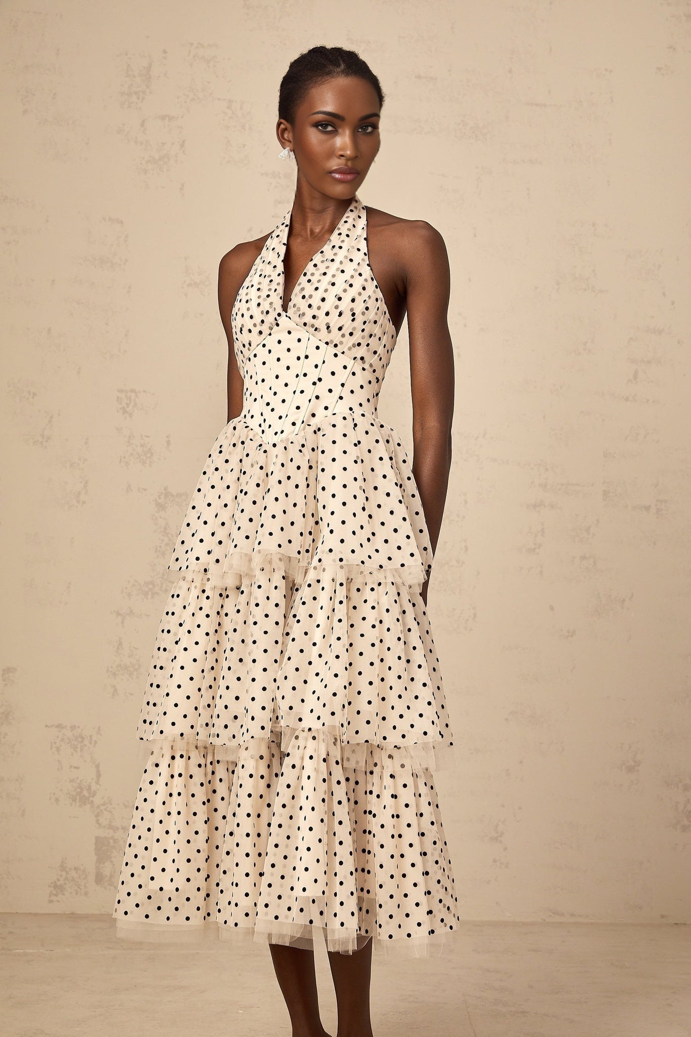 A white midi dress with small ivory polka dots featuring a tiered skirt and sleeveless design