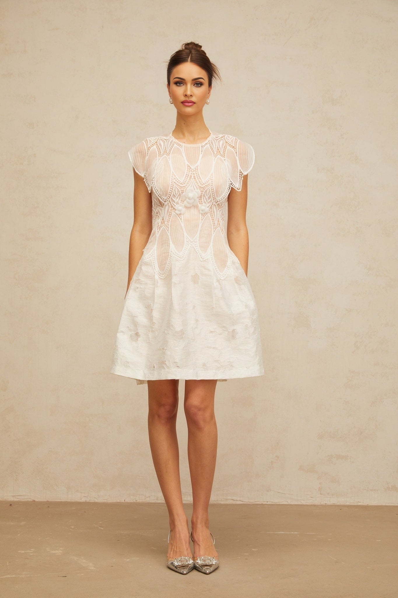 A white mini dress featuring three dimensional floral lace petals with corded details and a short hemline