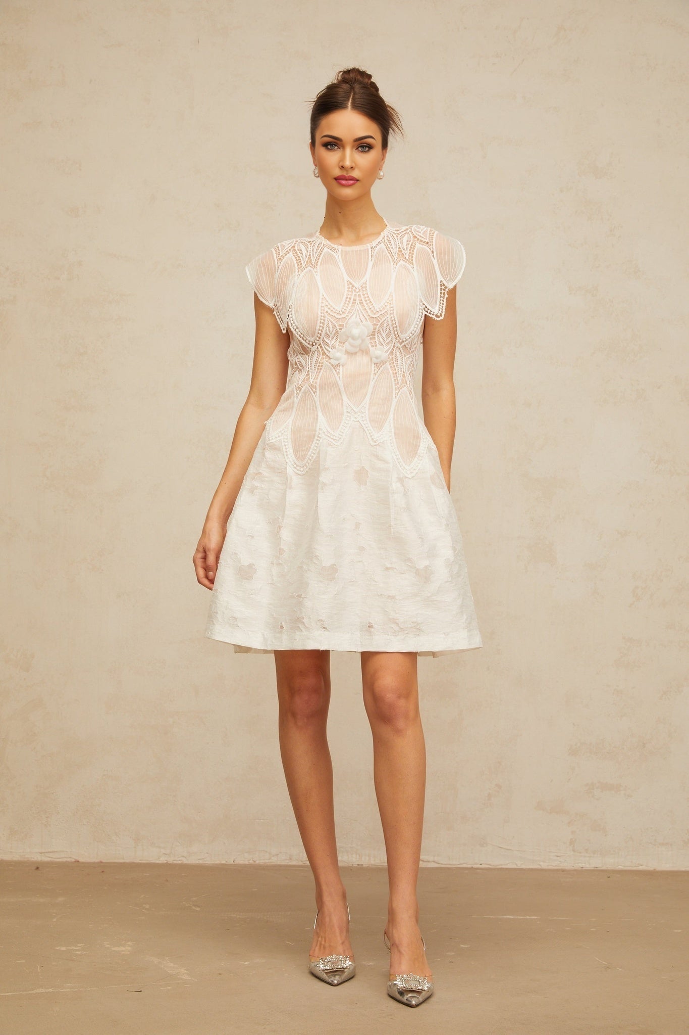 A white mini dress with a 3D floral pattern made of corded lace featuring petal details and a short hemline