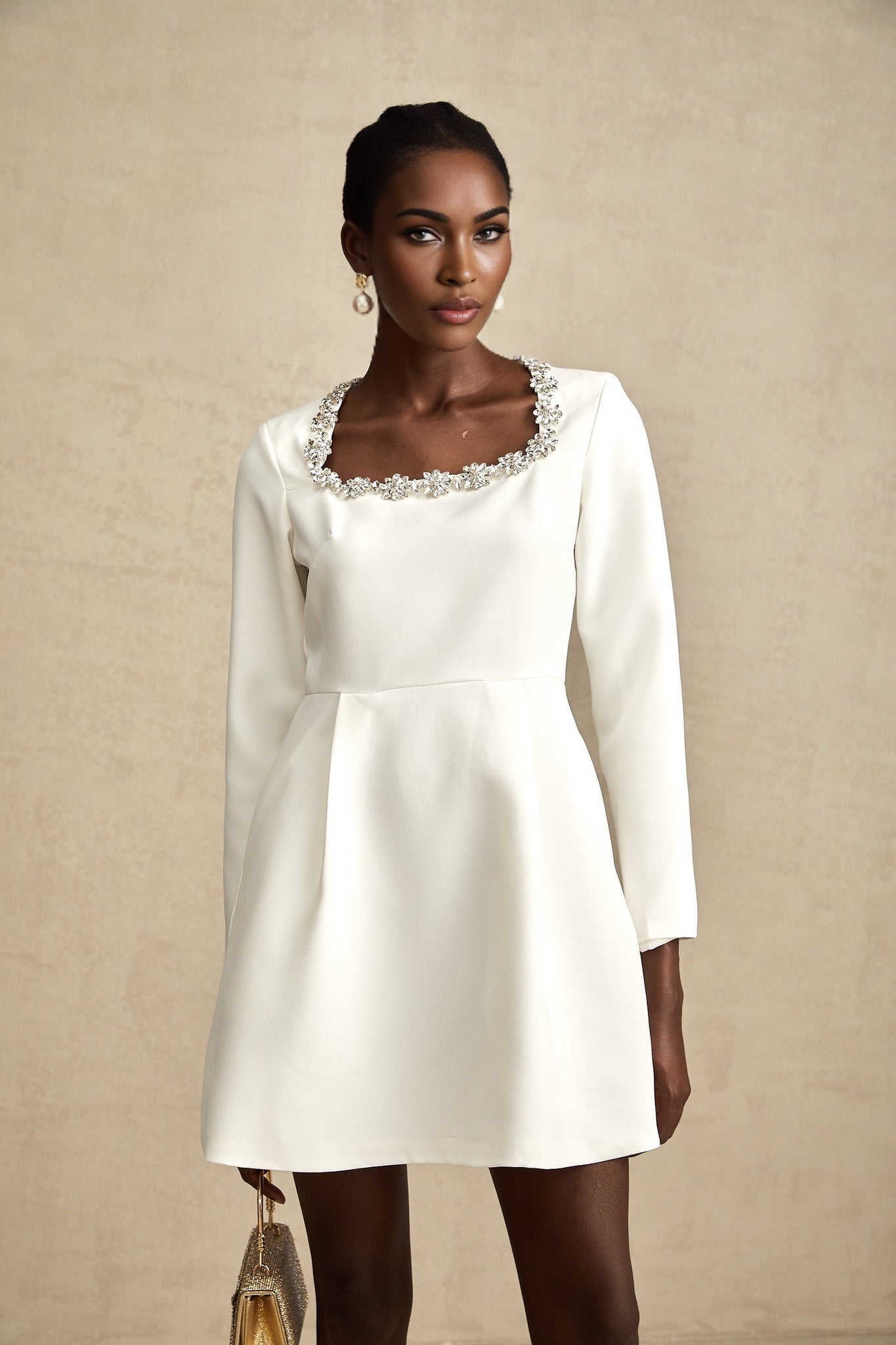 A white mini dress with a fitted bodice and flared Aline skirt adorned with crystal embellishments throughout featuring a sleeveless design and a short hemline
