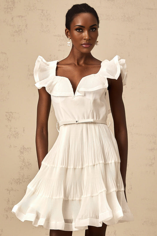 A white mini dress with a frilled neckline and pleated skirt worn by a model standing against a plain background