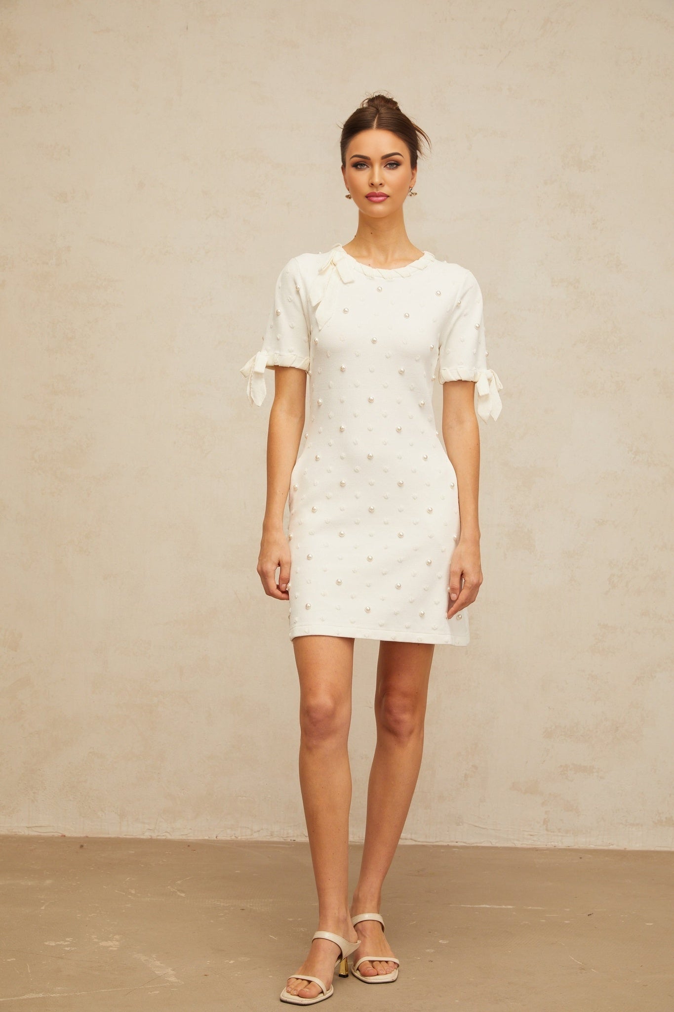 A white mini dress with black polka dots and heart patterns knitted into the fabric featuring short sleeves and a fitted silhouette